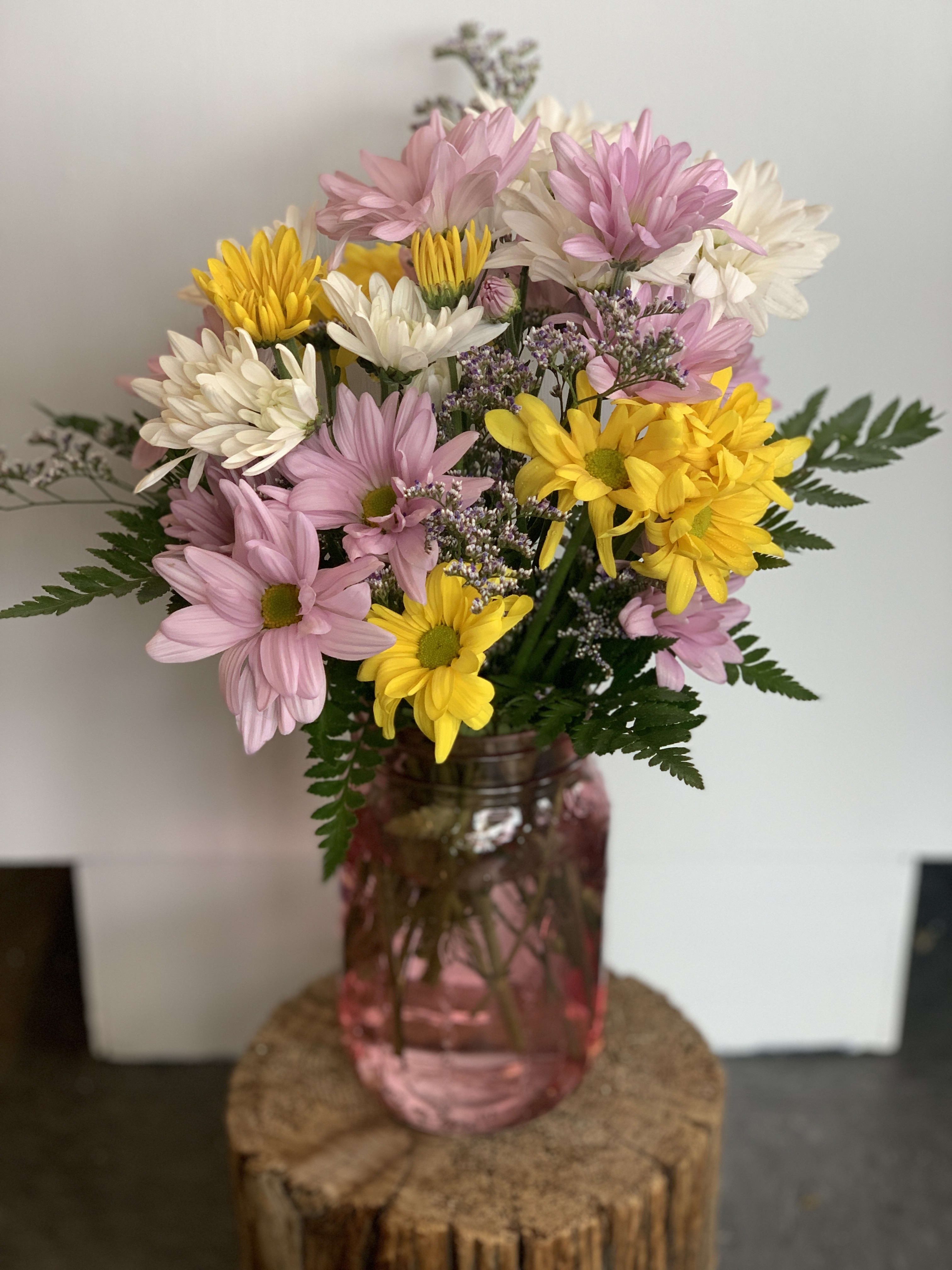 Pink, white, and yellow daisy bouquet in a pink glass vase