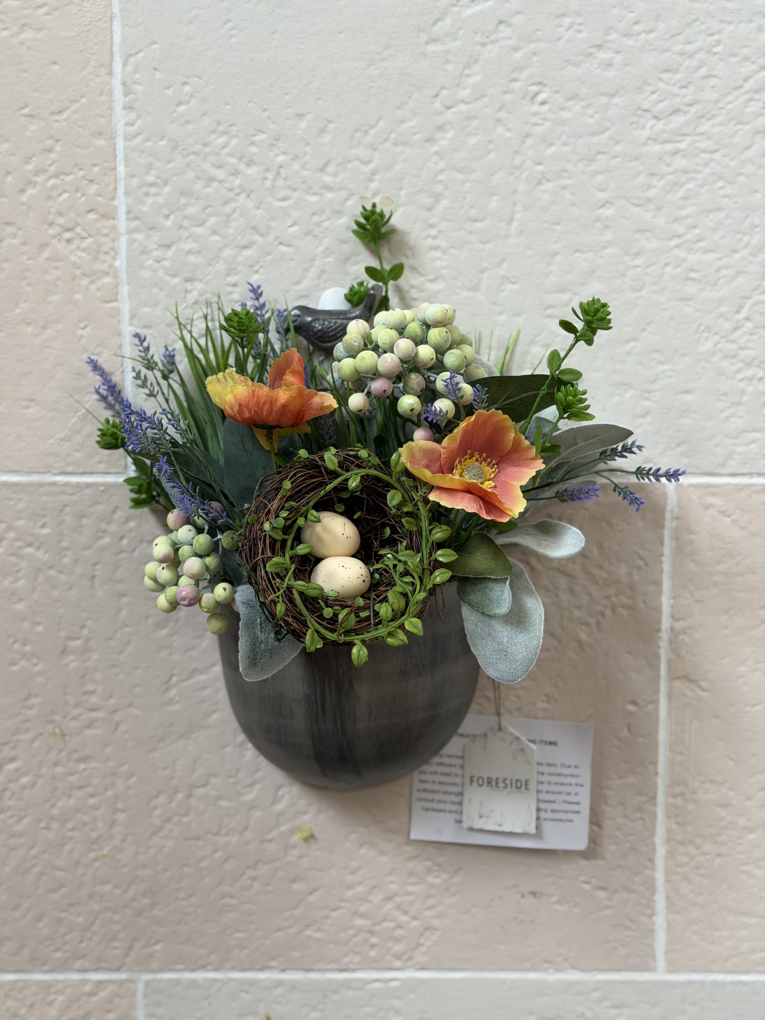 Metal Bird Artificial Arrangement  - A wild flower style artificial arrangement with an artificial birds nest in a wall decor style container with a bird on the hanger. 