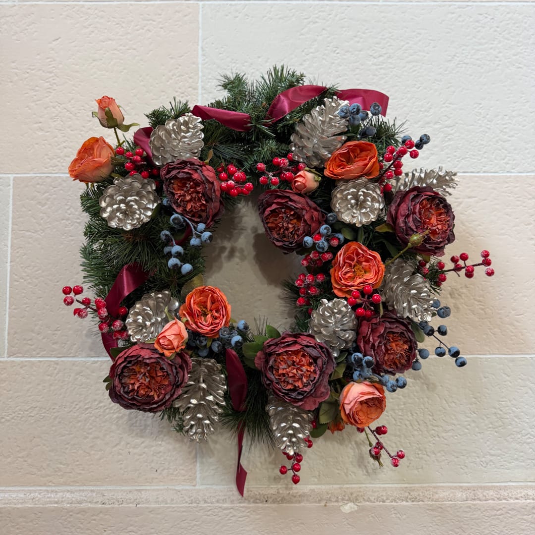 Holiday wreath with orange roses, berries, and silver pinecones on a wall