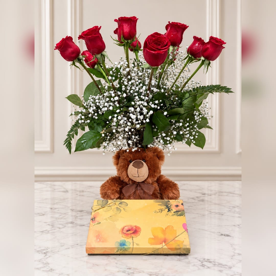 Red roses arranged above a teddy bear and floral gift box