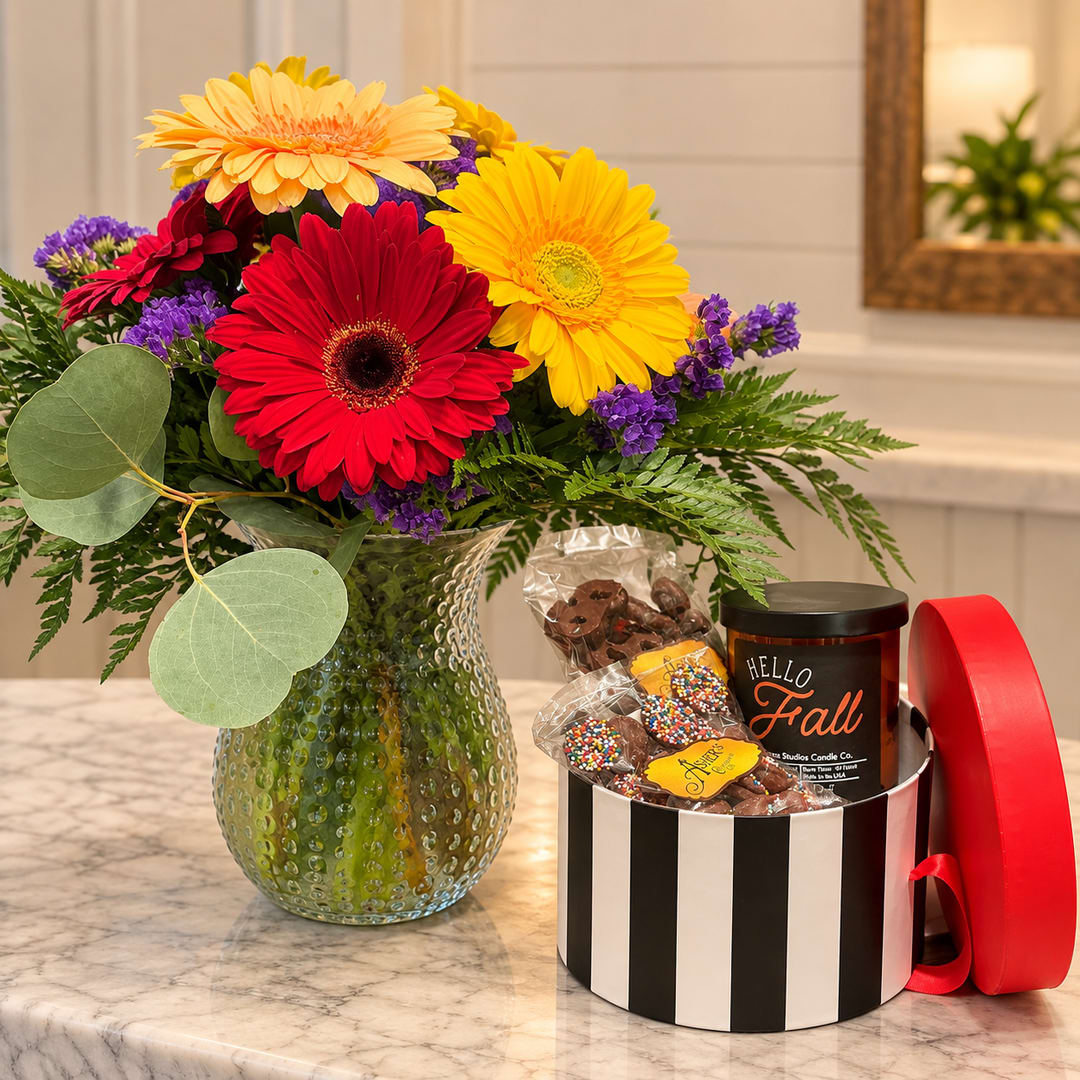 Colorful gerbera bouquet in a textured glass vase beside a candy gift box