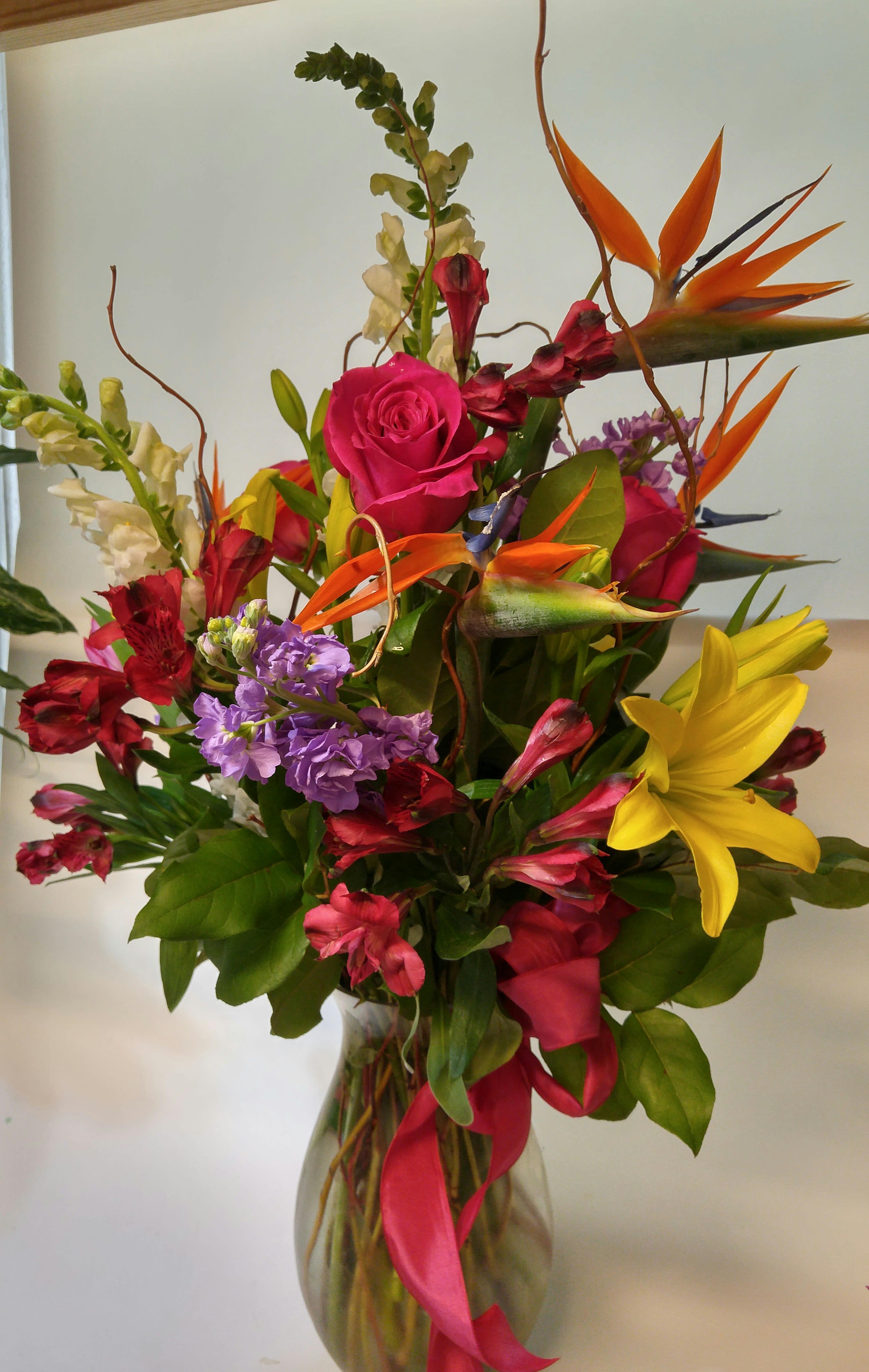 Mixed bouquet with roses, lilies, and bird-of-paradise in a glass vase