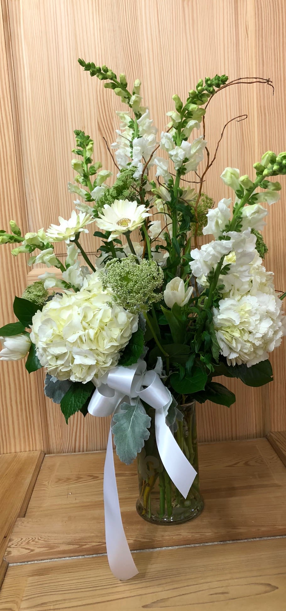 White floral arrangement in a glass vase with a white ribbon