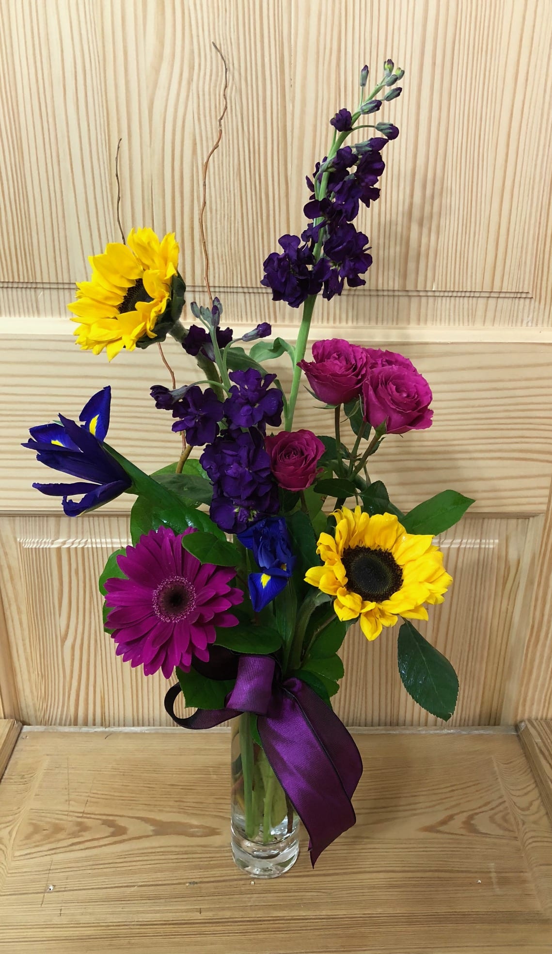 Colorful mixed bouquet in a clear glass vase with a purple ribbon