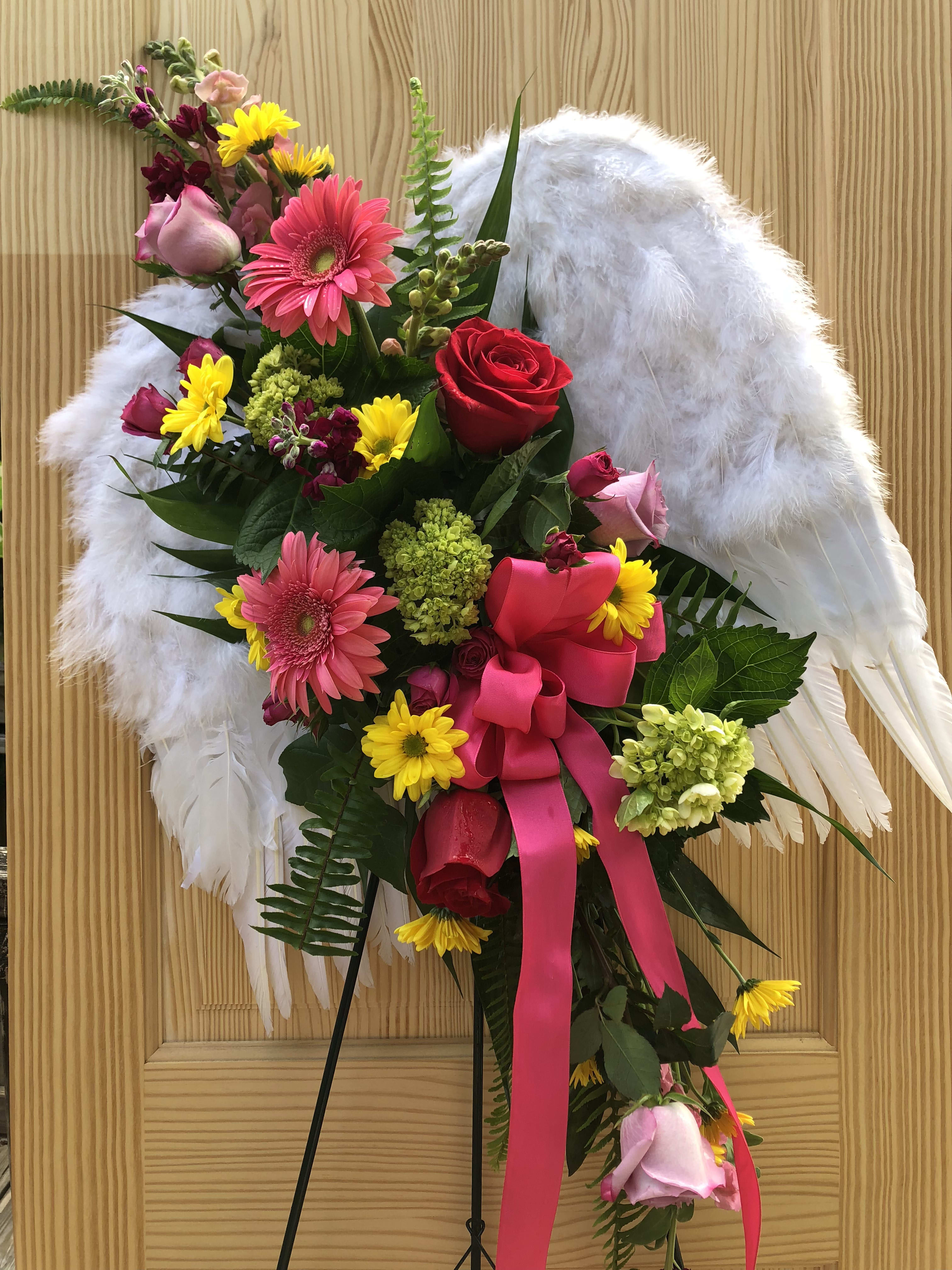 Floral standing spray with pink and red roses, gerbera daisies, and white wings