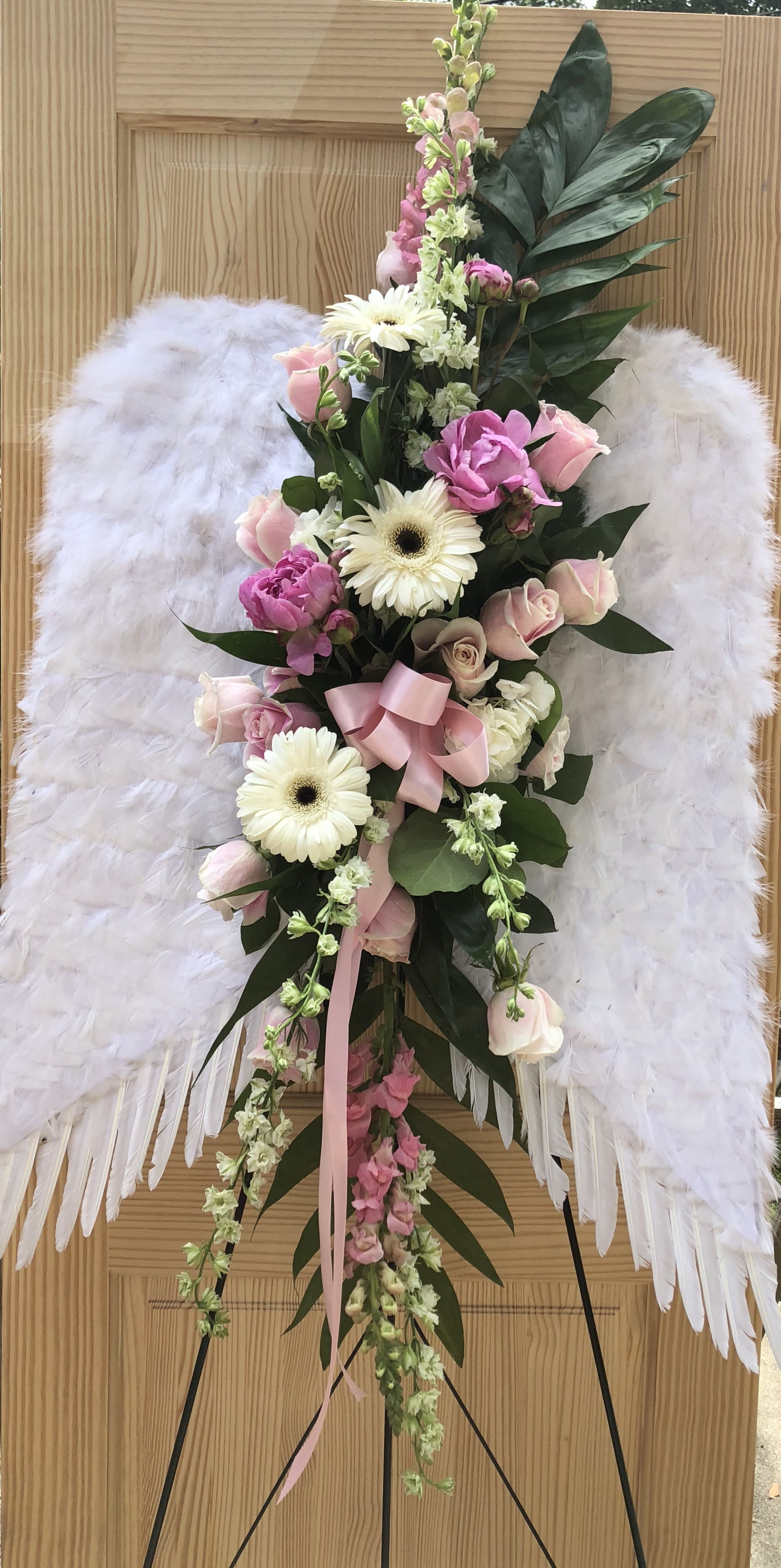 White angel wings with a pink and white floral spray on a stand
