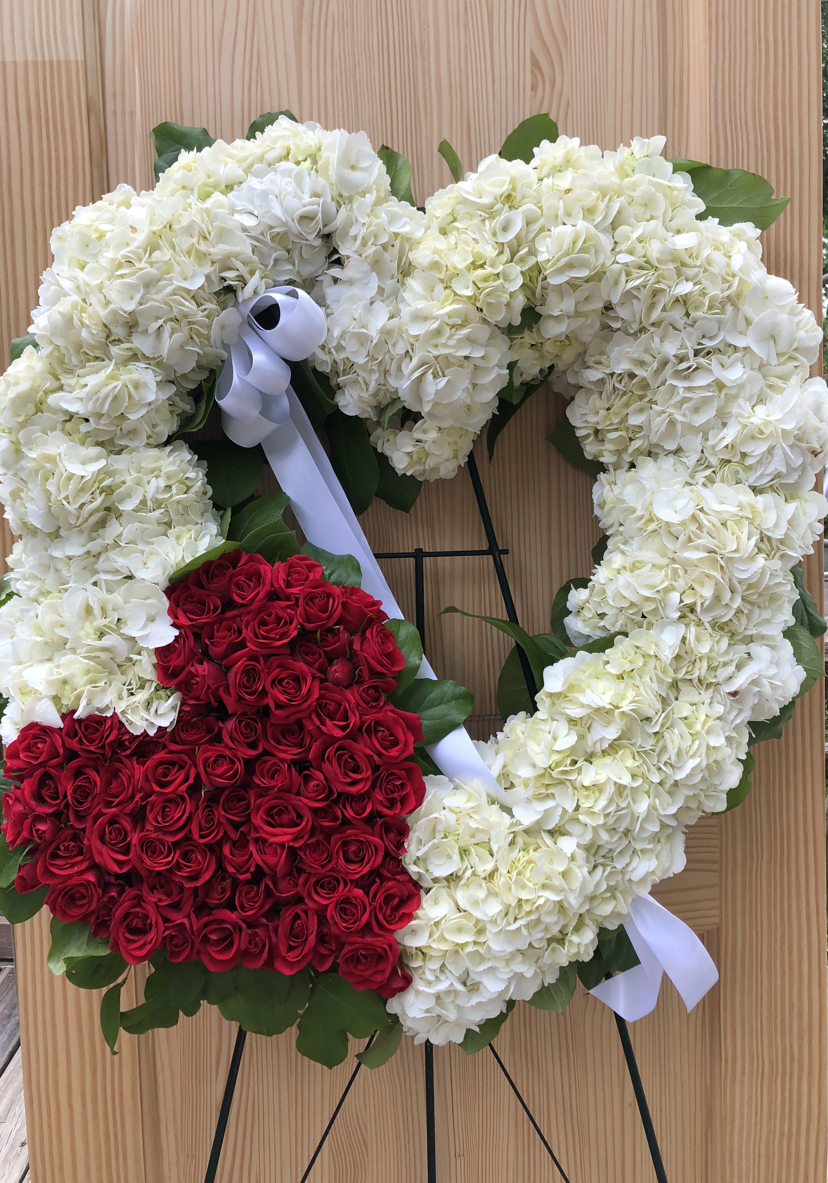 Heart-shaped floral wreath with white hydrangeas and red roses on a stand