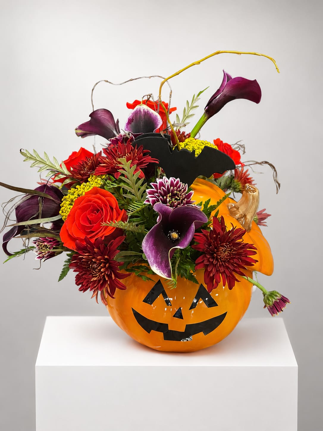 Halloween pumpkin container filled with purple calla lilies and red flowers