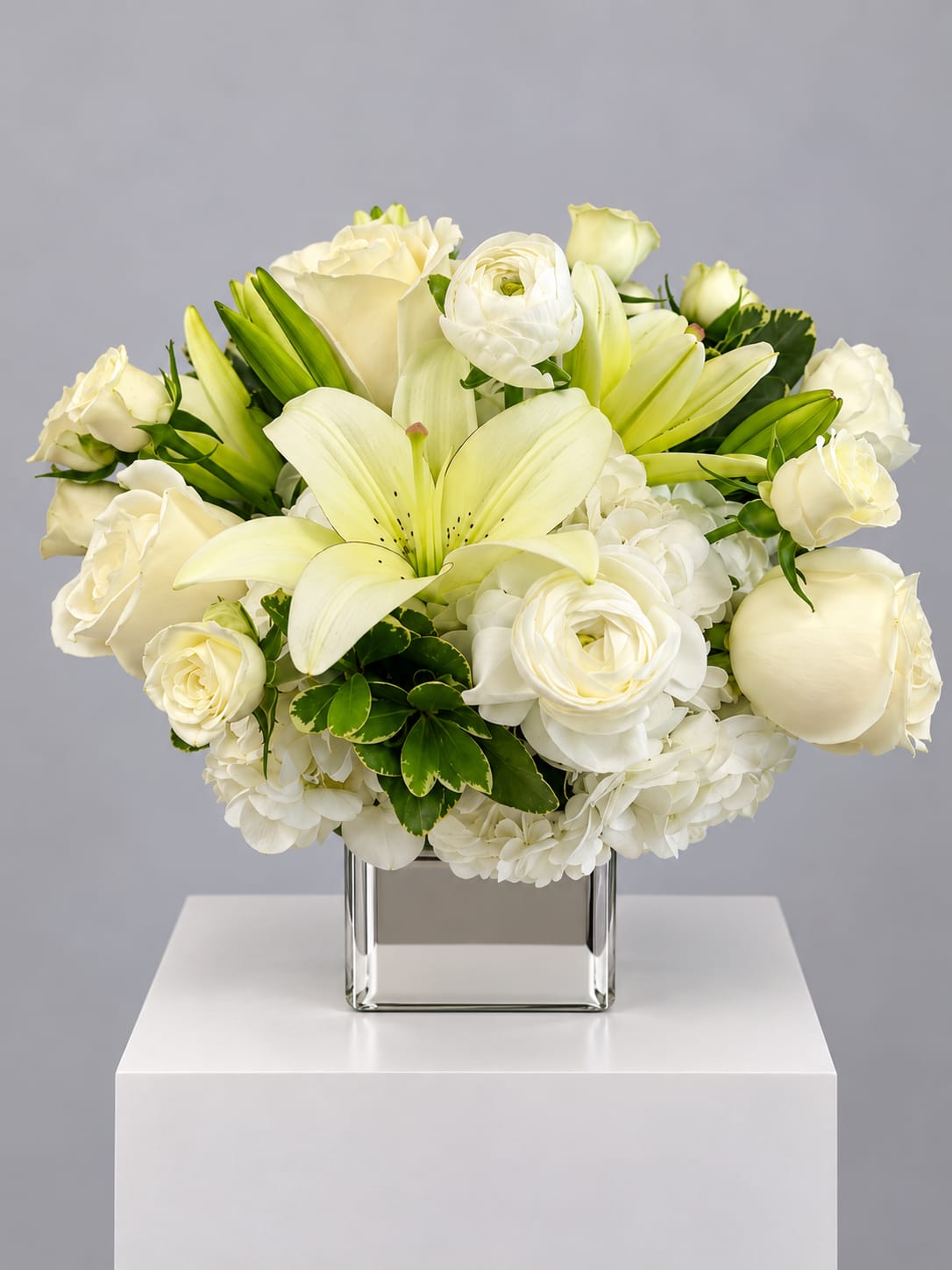 White roses and lilies arranged in a square glass vase
