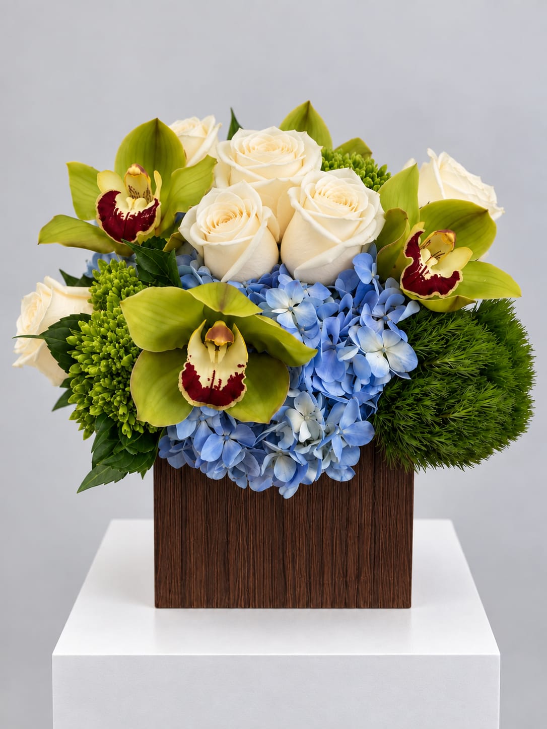 White roses, blue hydrangeas, and green orchids in a square wooden vase