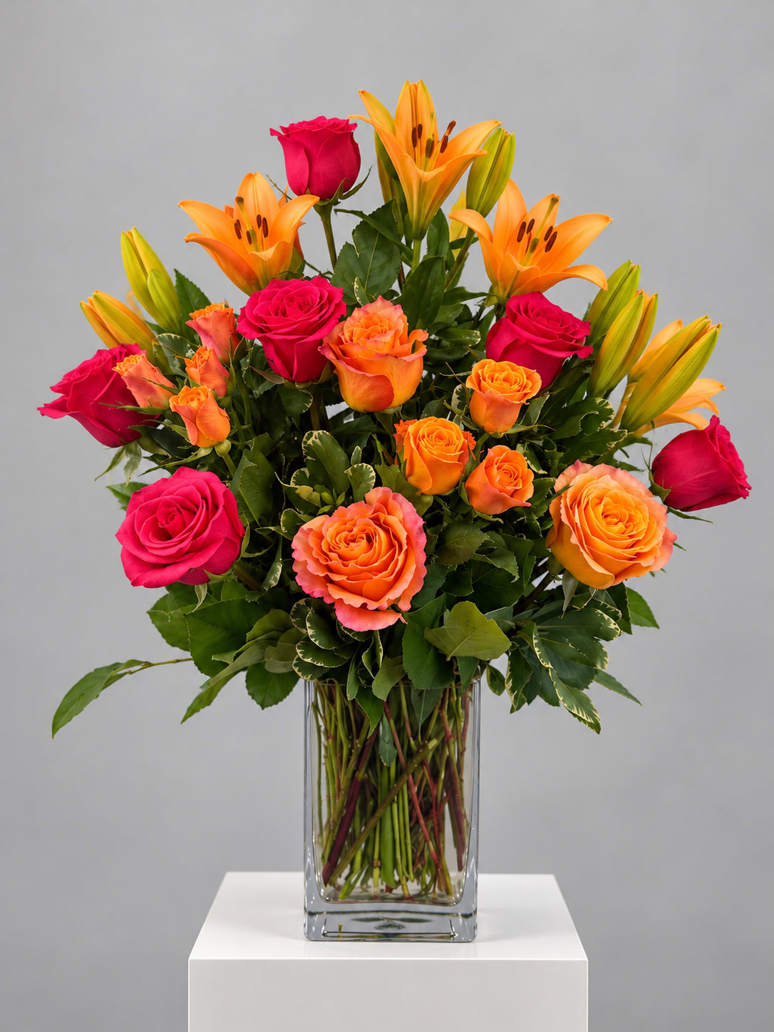 Pink and orange roses with orange lilies in a glass vase