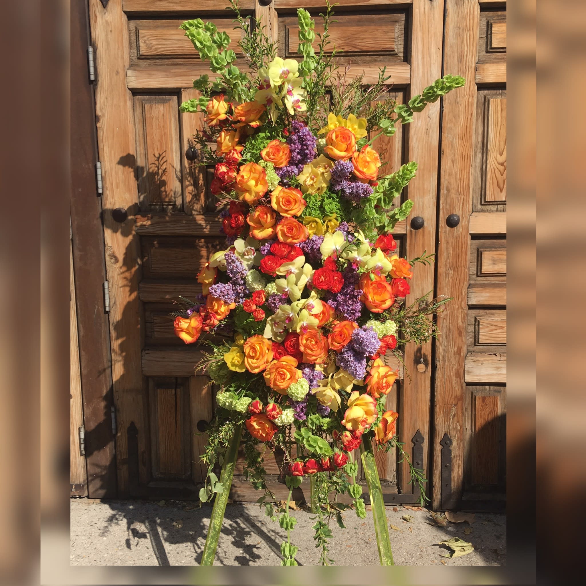 Tall floral standing spray on an easel with orange, yellow, red, and purple blooms