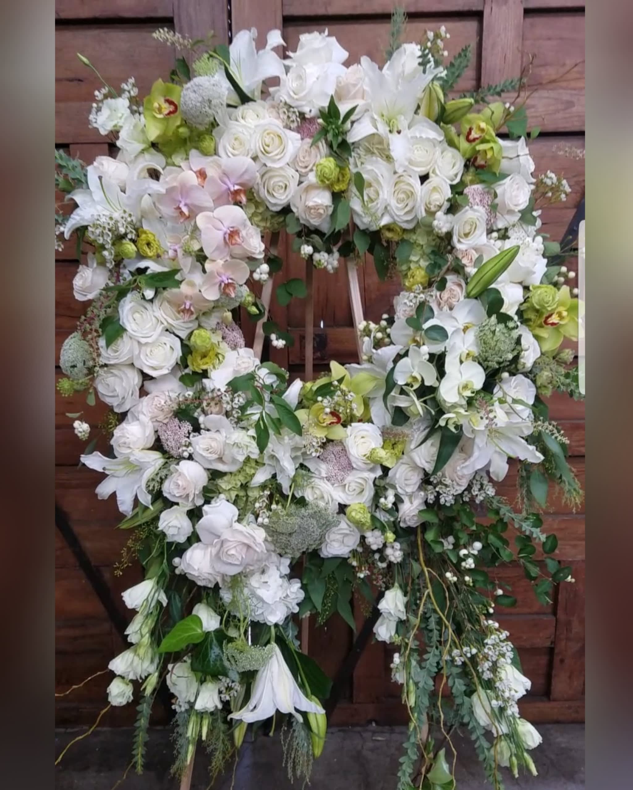Large floral wreath of white roses, orchids, and lilies on an easel