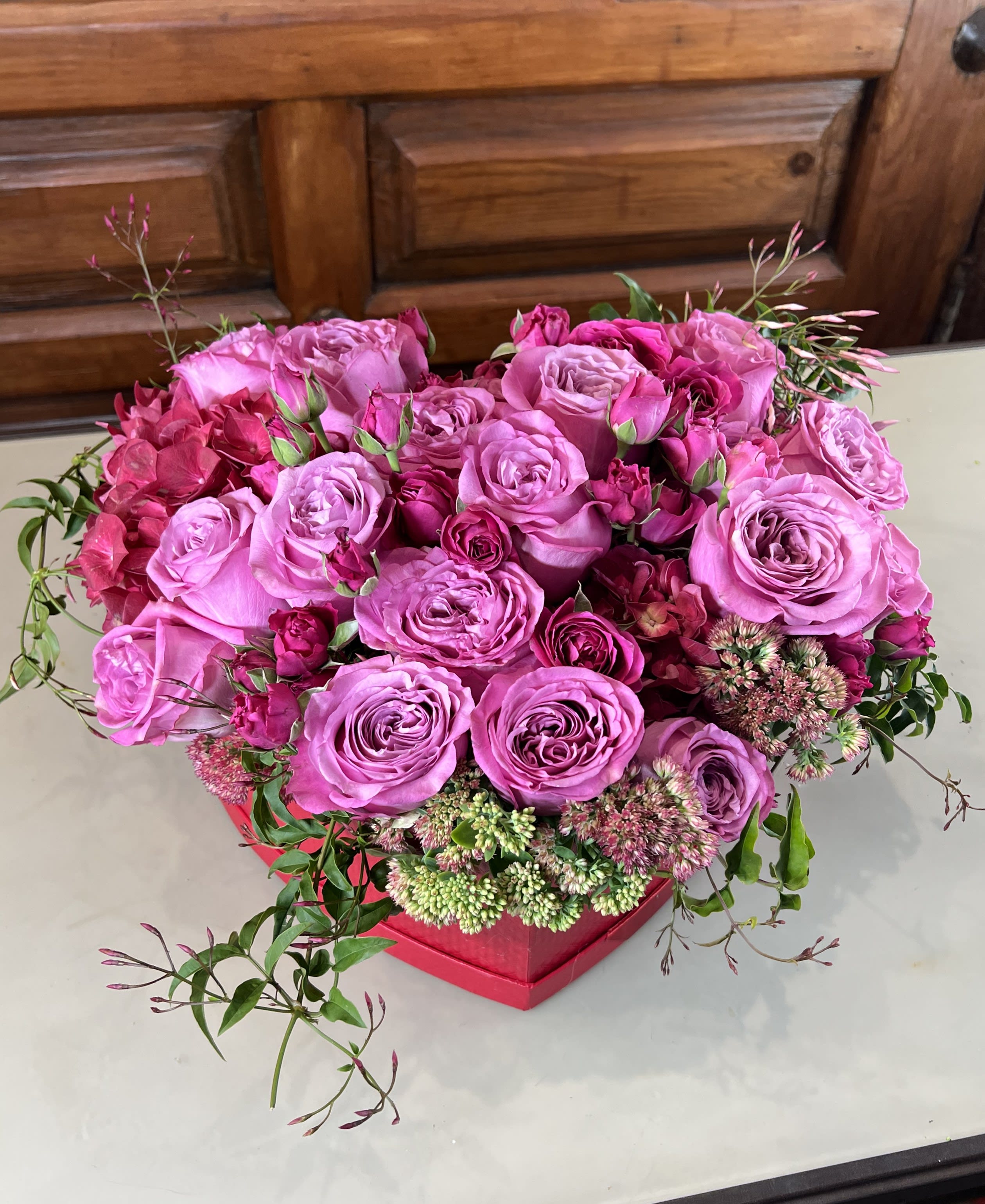 Pink rose arrangement in a red box with small accent flowers