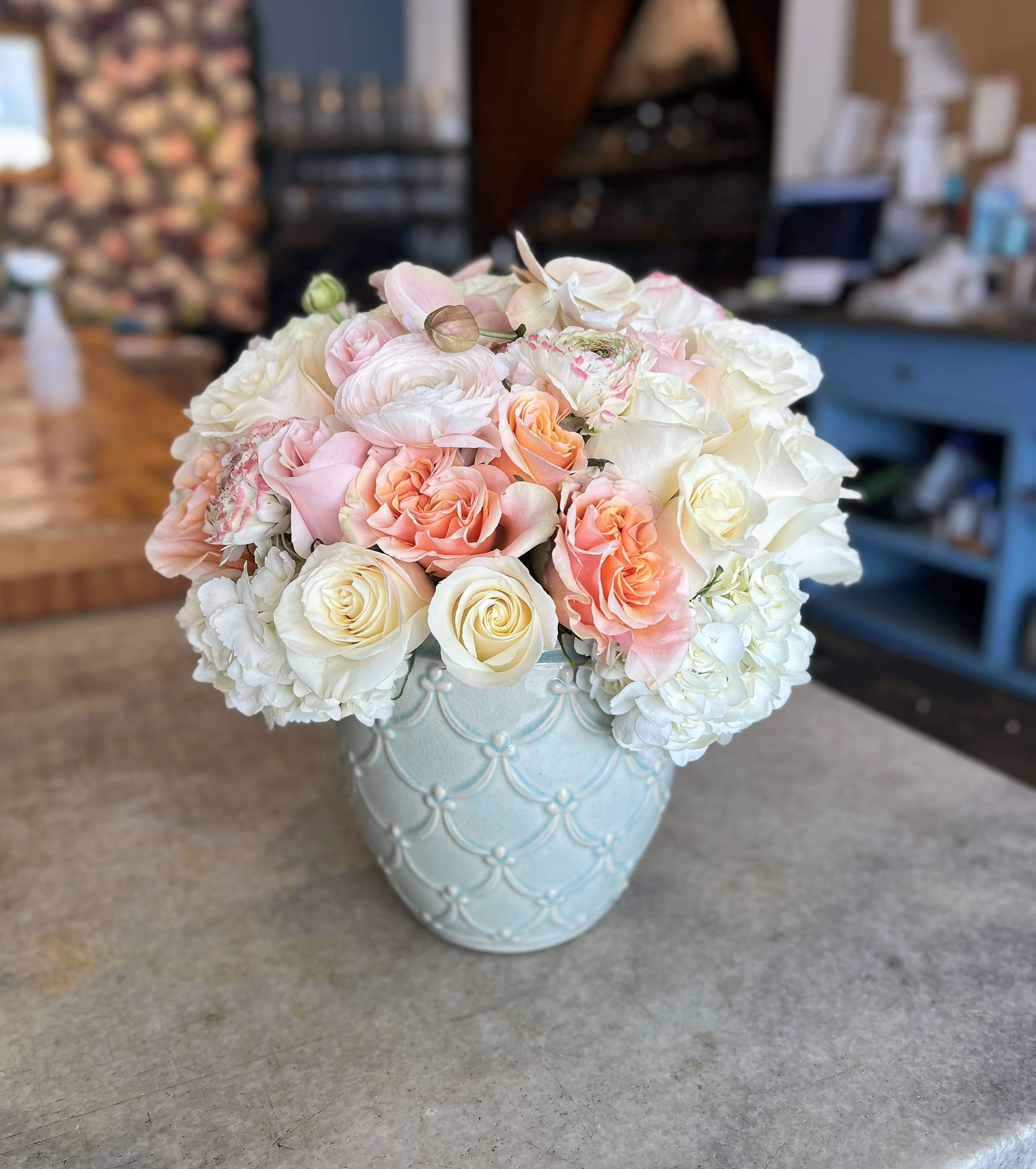 Pastel roses and white blooms arranged in a light blue vase