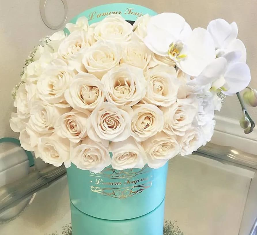 White roses and orchids arranged in a turquoise hat box