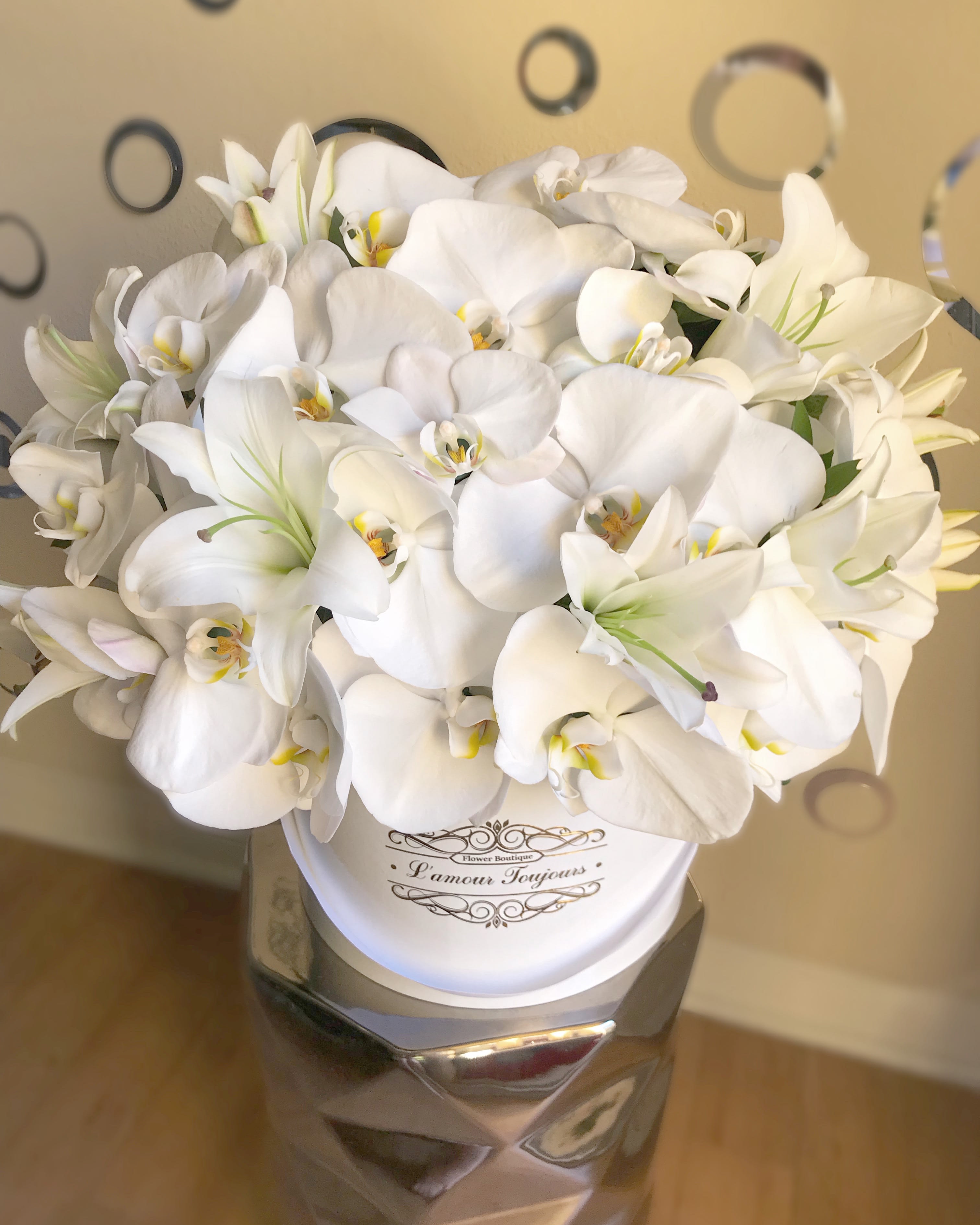 Round white hatbox filled with white orchids and lilies on a metallic pedestal stand