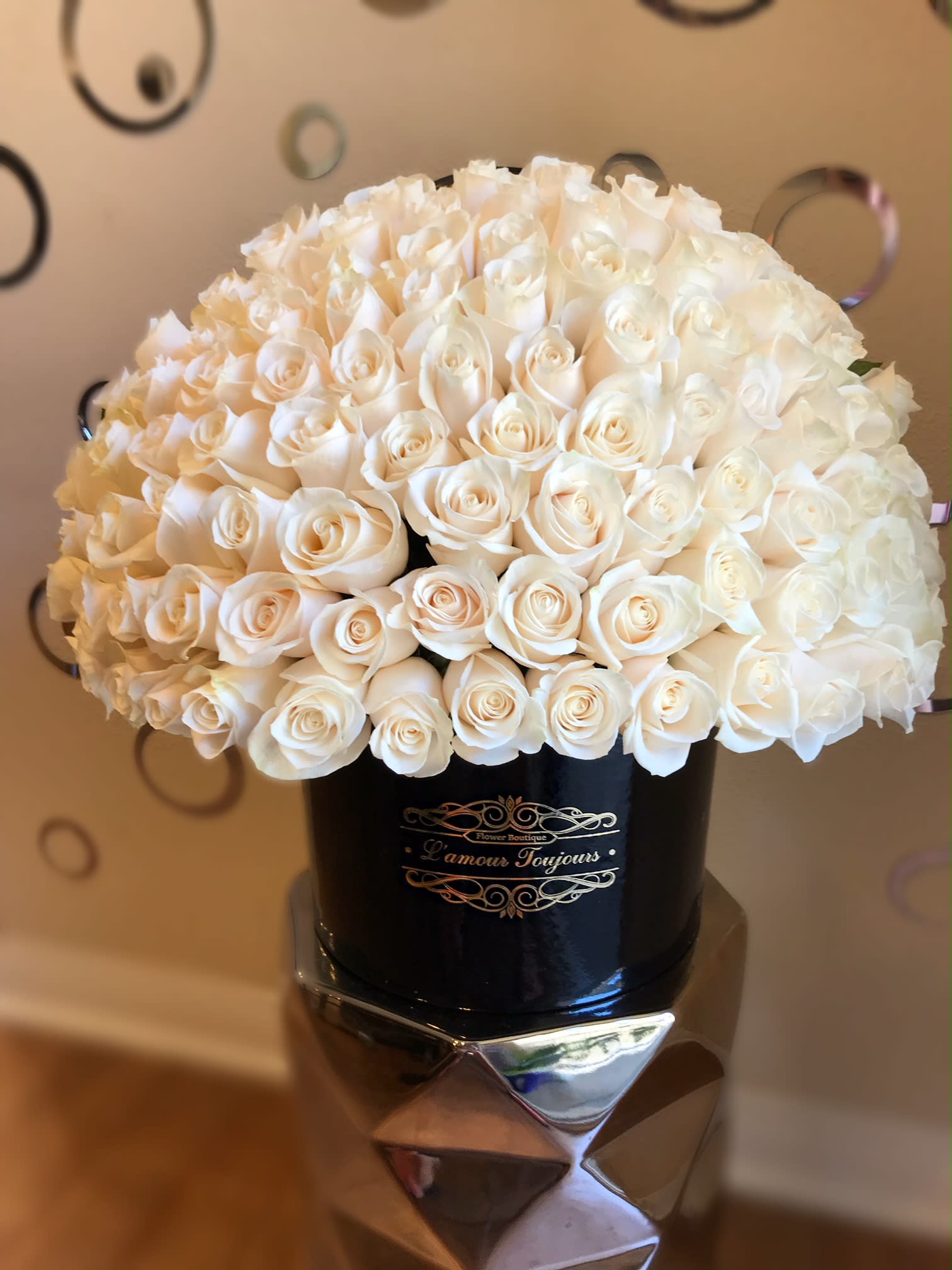 Dome of ivory roses arranged tightly in a black round hat box with gold lettering