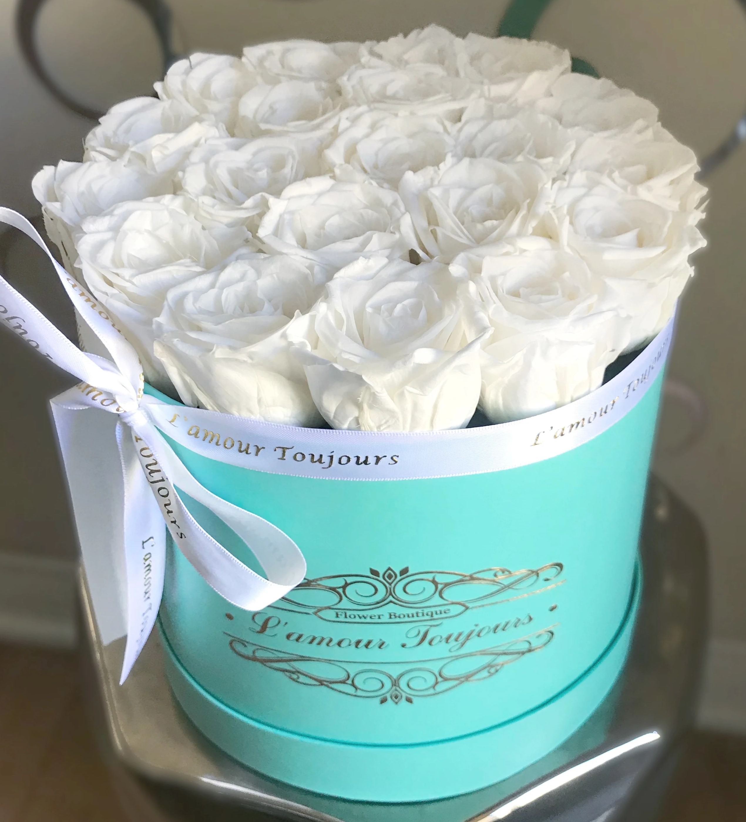 White roses arranged in a turquoise round box with a white ribbon