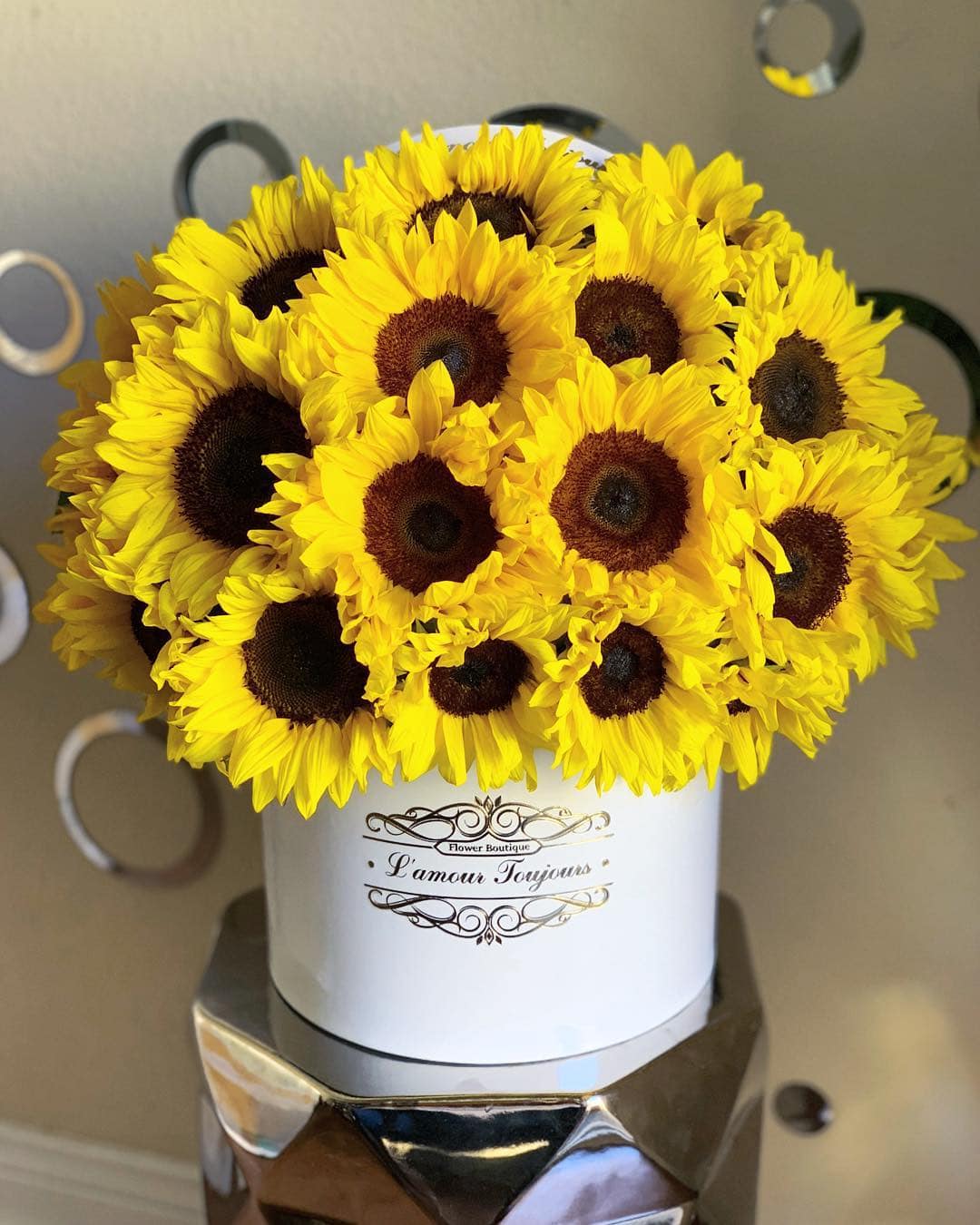 Hat box arrangement of bright yellow sunflowers with dark centers in a white cylinder container