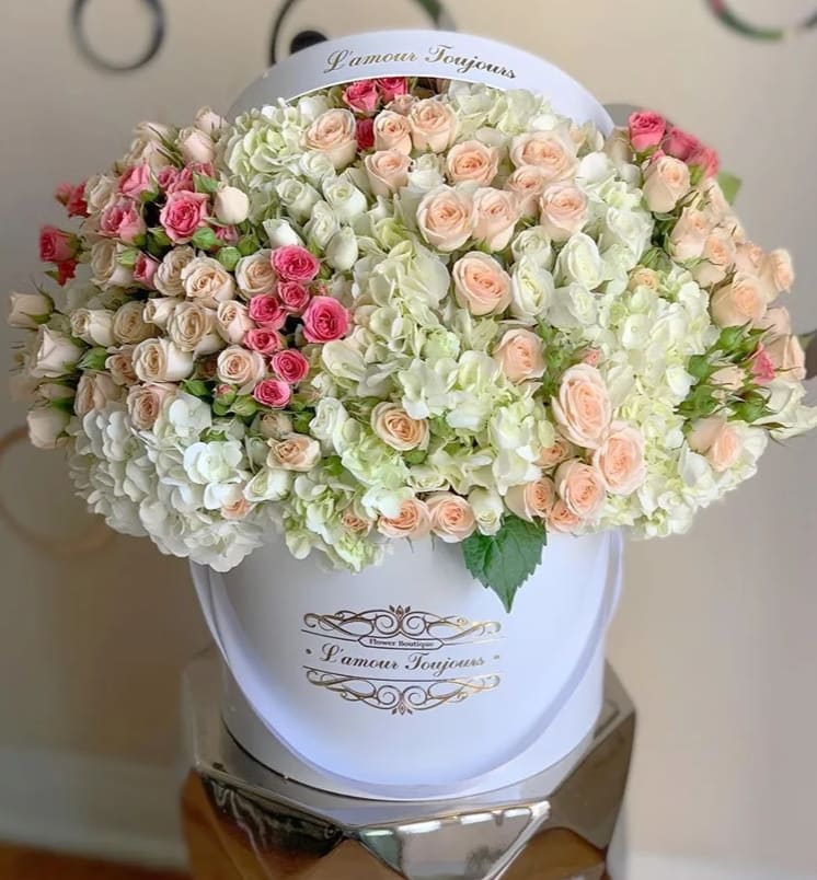 Large hatbox arrangement of pastel roses and white hydrangeas in a white container.