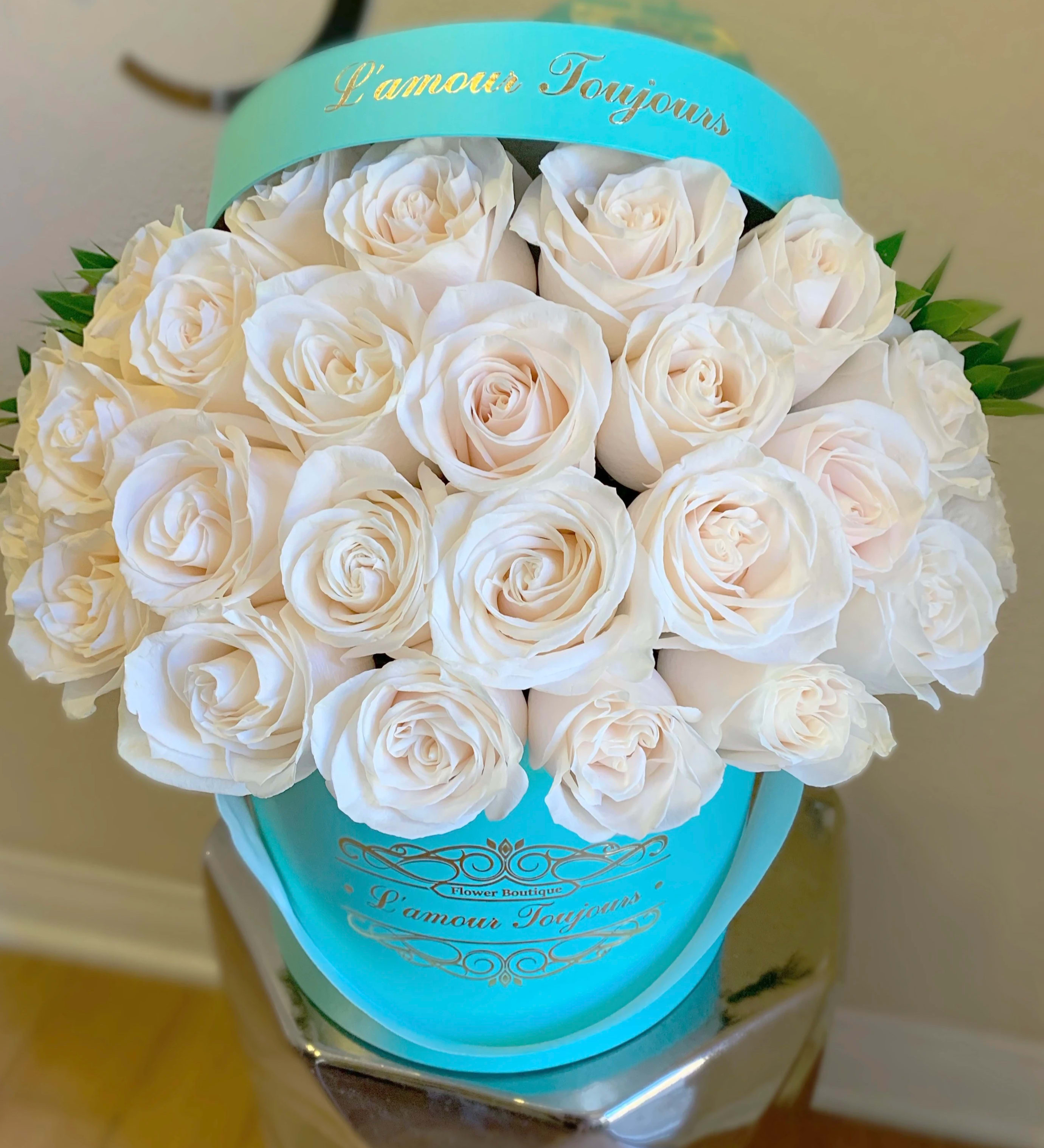 White roses arranged in a turquoise hatbox with gold lettering.