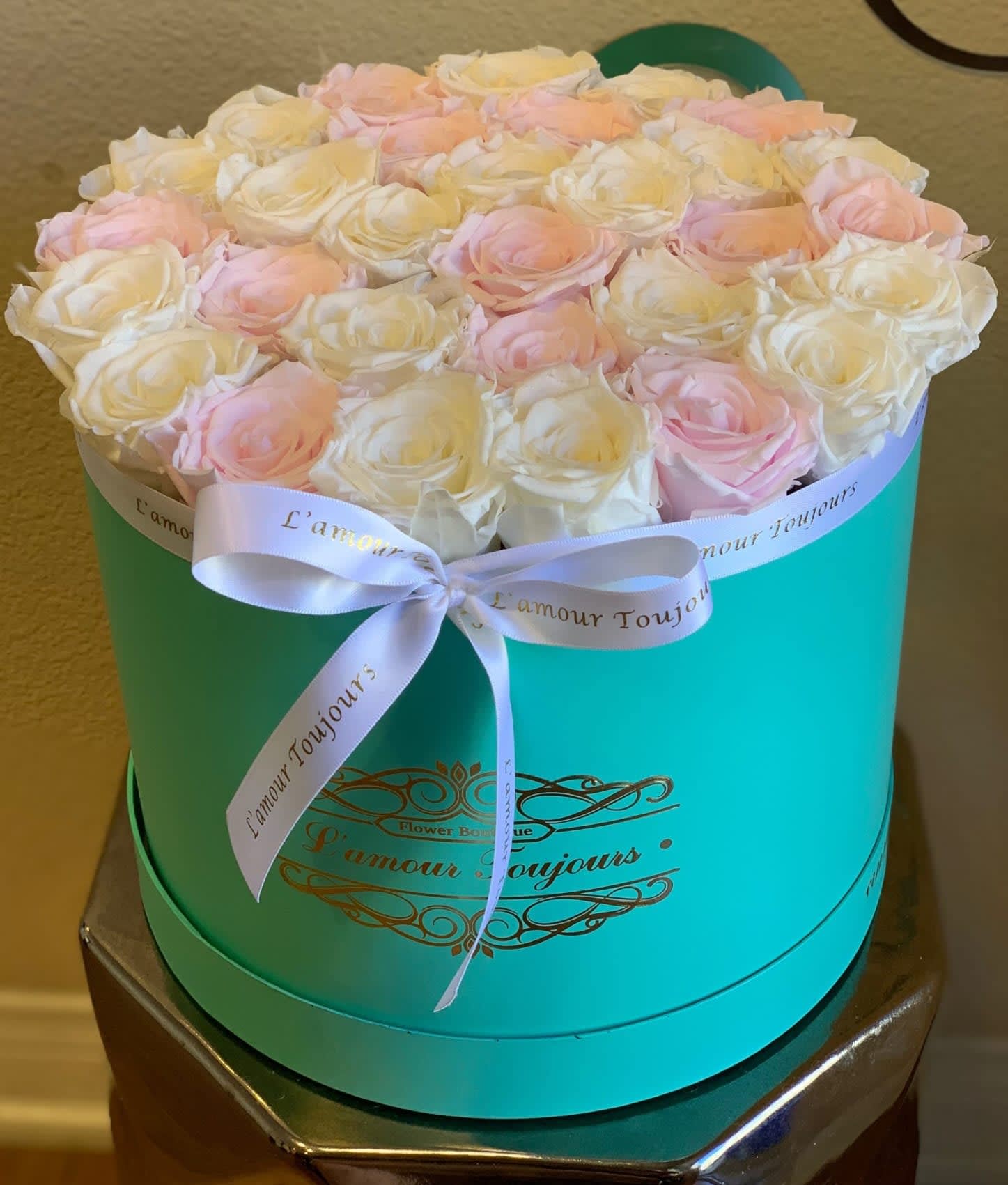 Pink and white roses arranged in a turquoise round box with a ribbon