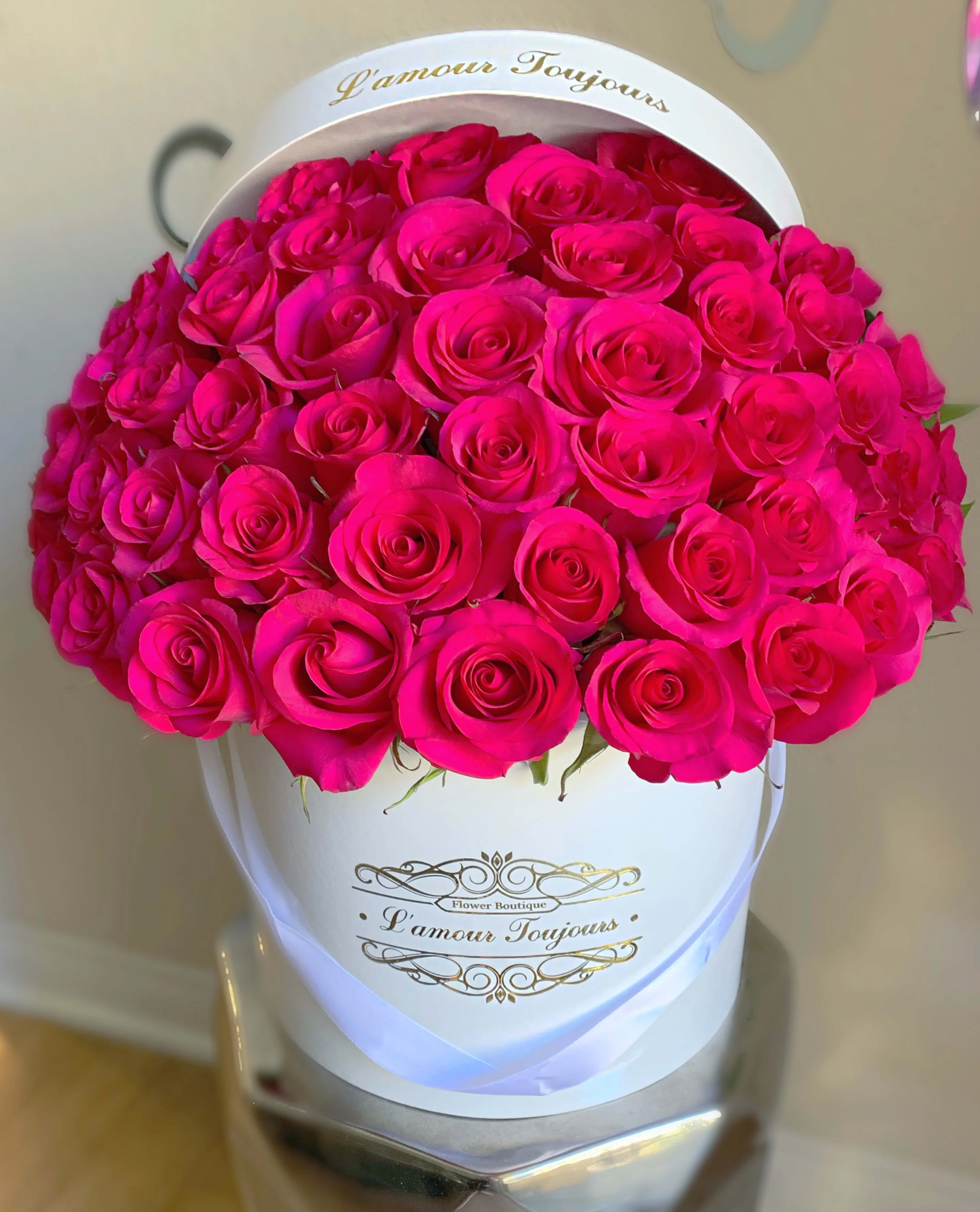 Hot pink roses densely arranged in a white hatbox-style container with gold script text