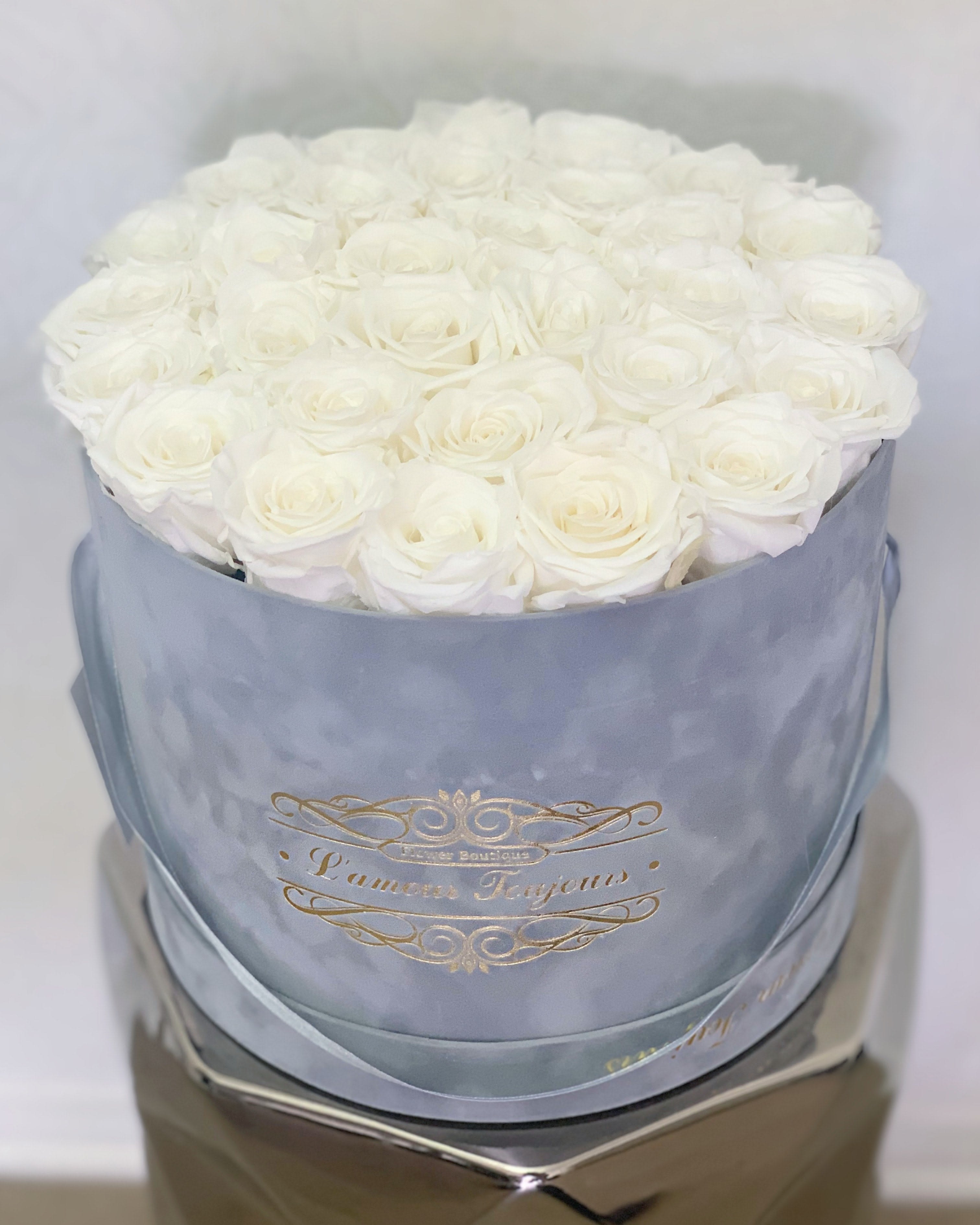 Round box filled with tightly packed white roses in a light blue container