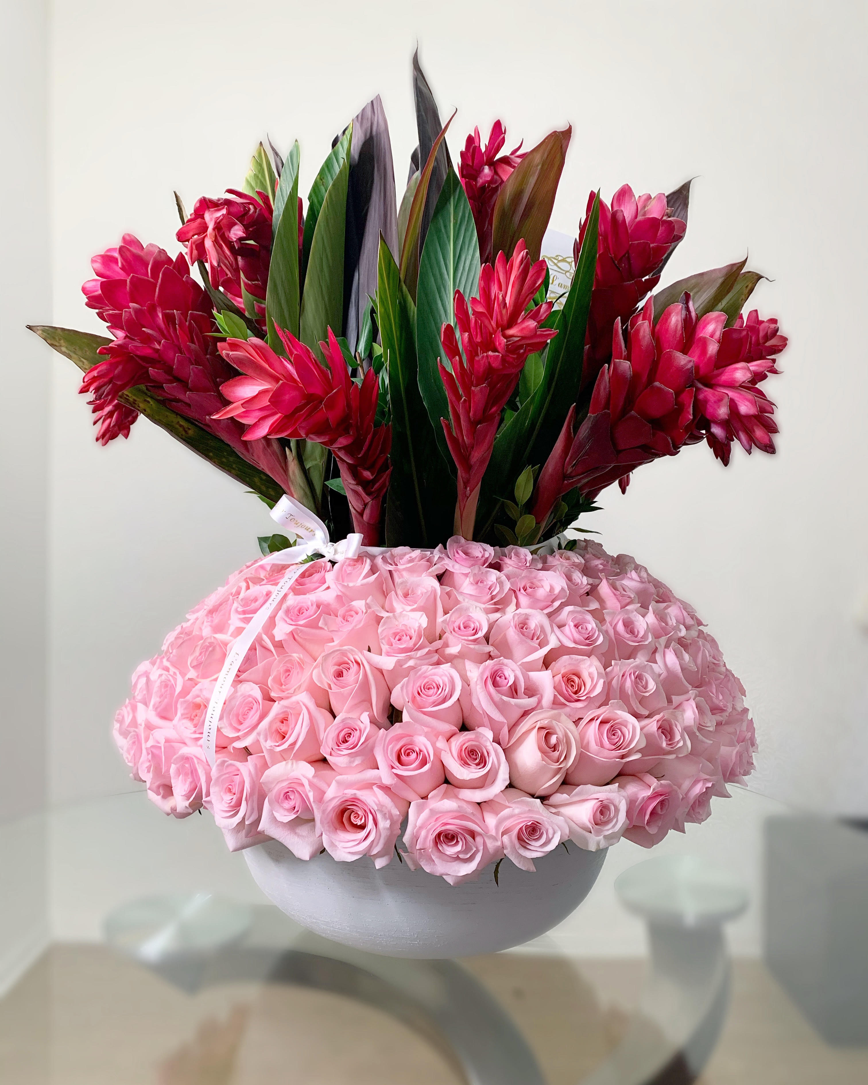 Pink roses in a white bowl with red tropical flowers above