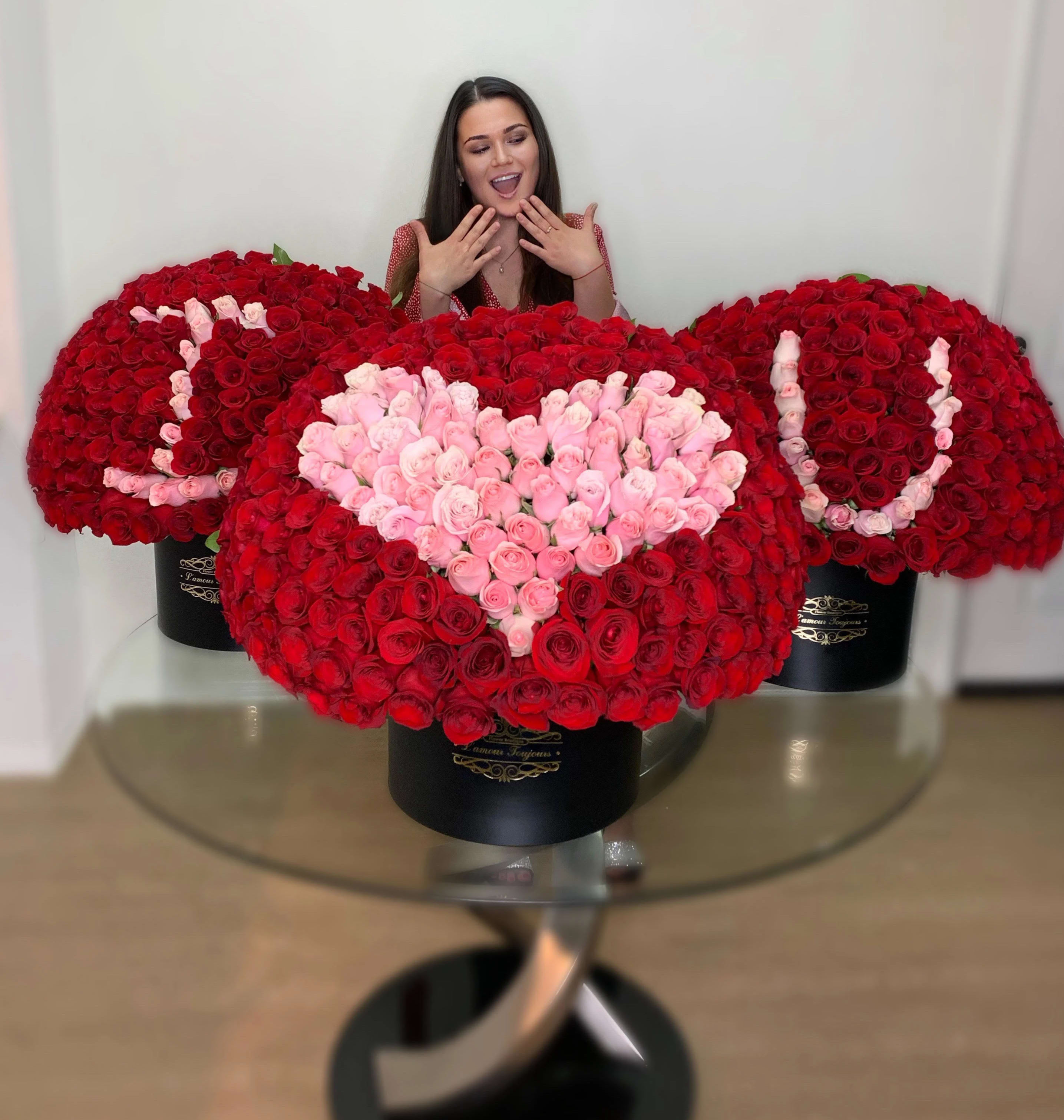 Three large red and pink rose hatbox arrangements spelling I heart U on a glass table