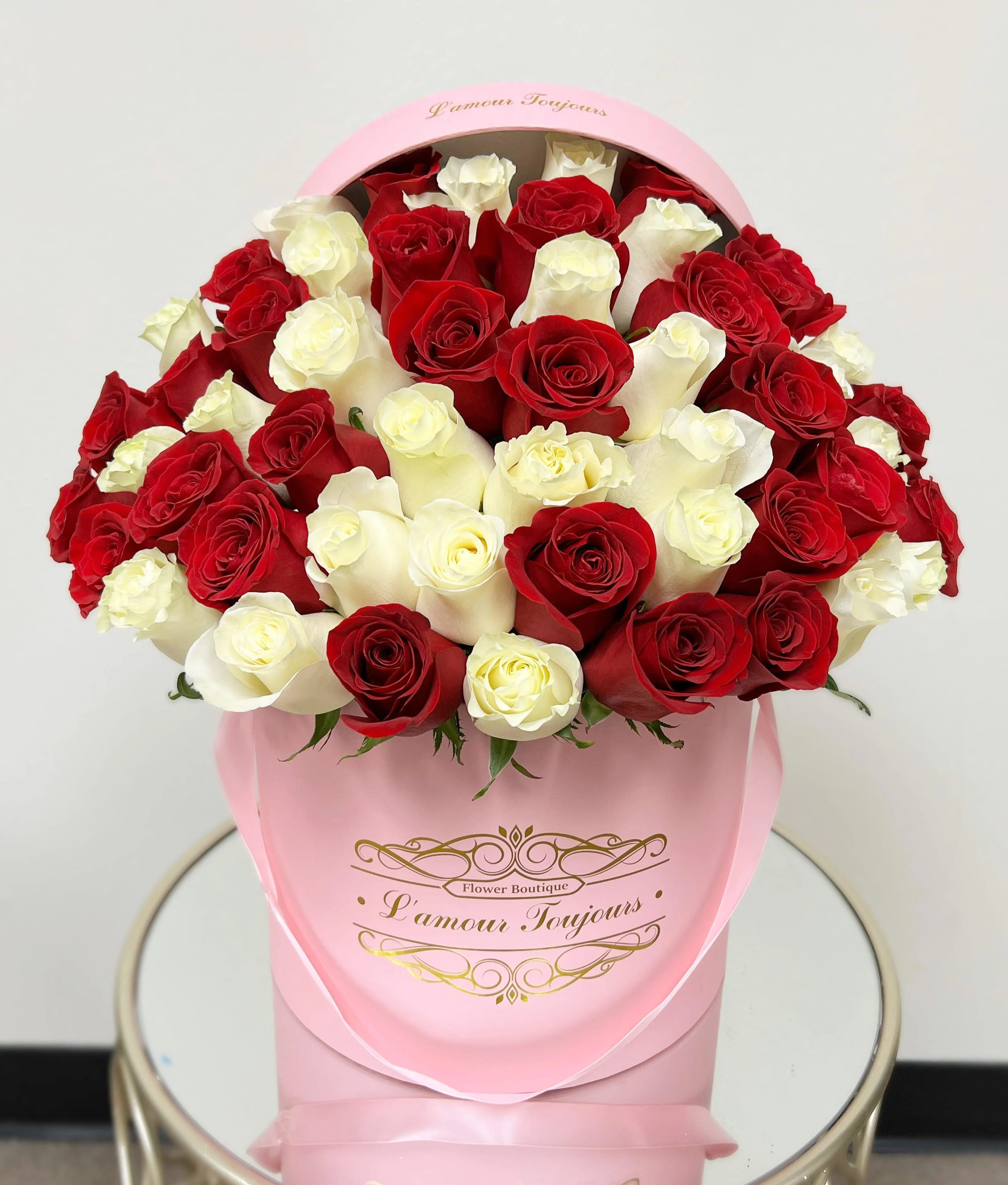 Red and white roses arranged in a pink hatbox on a small round table.