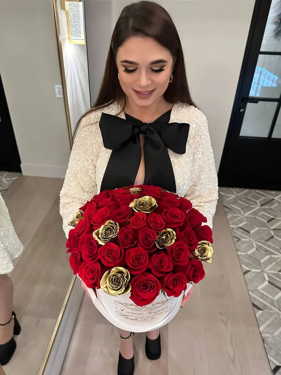 Round box of red and gold roses held in front of a woman in a dress