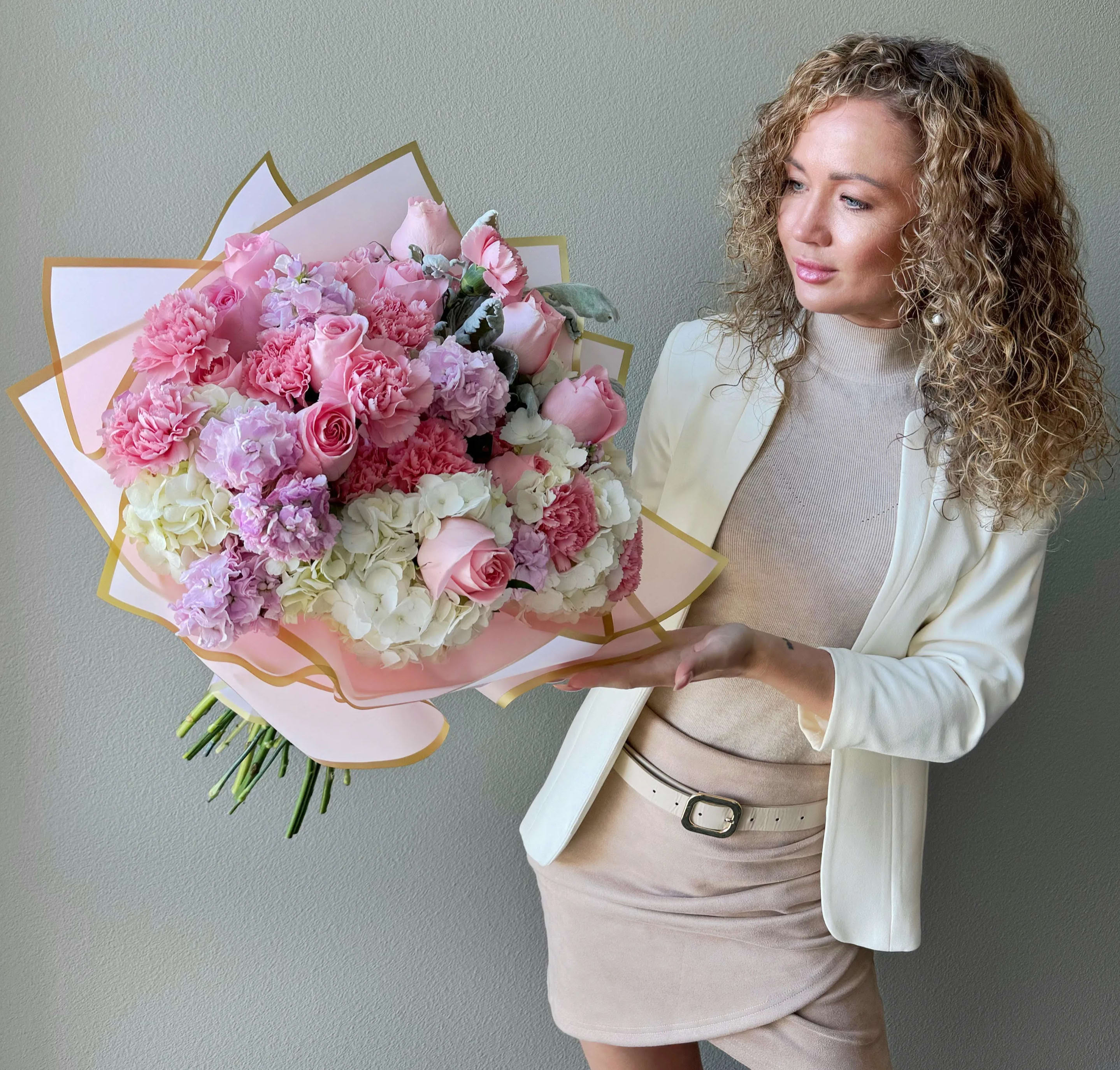 Large pink and white bouquet with roses and carnations held by a woman in a cream outfit