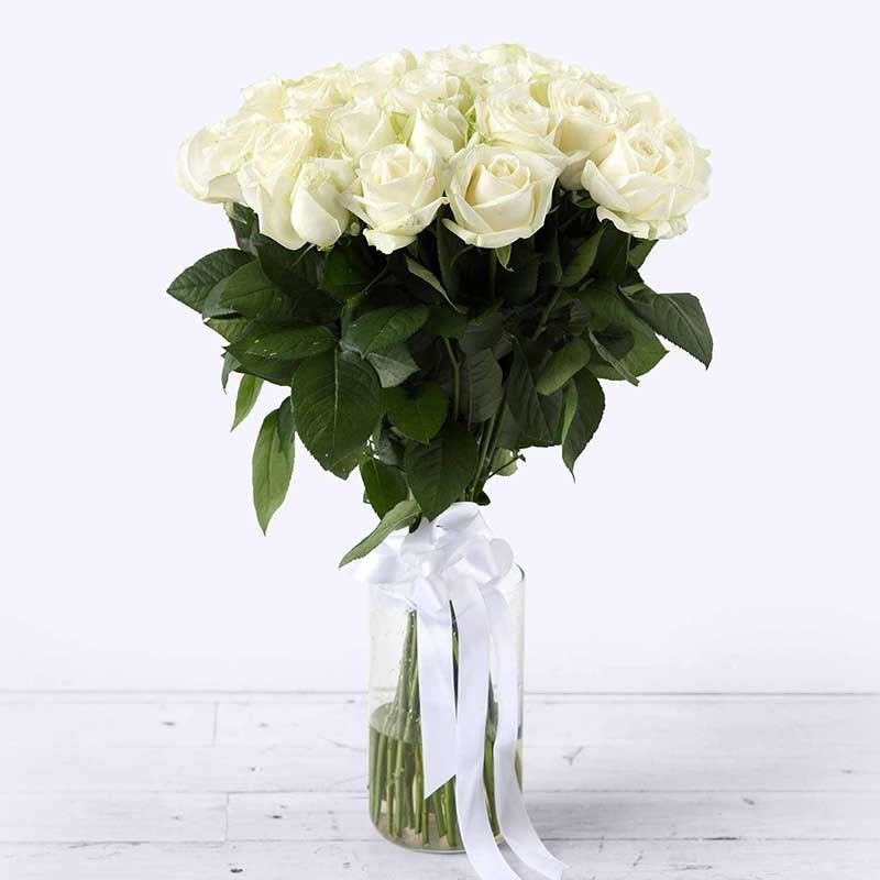Tall arrangement of white roses in a clear glass vase with a white ribbon bow.