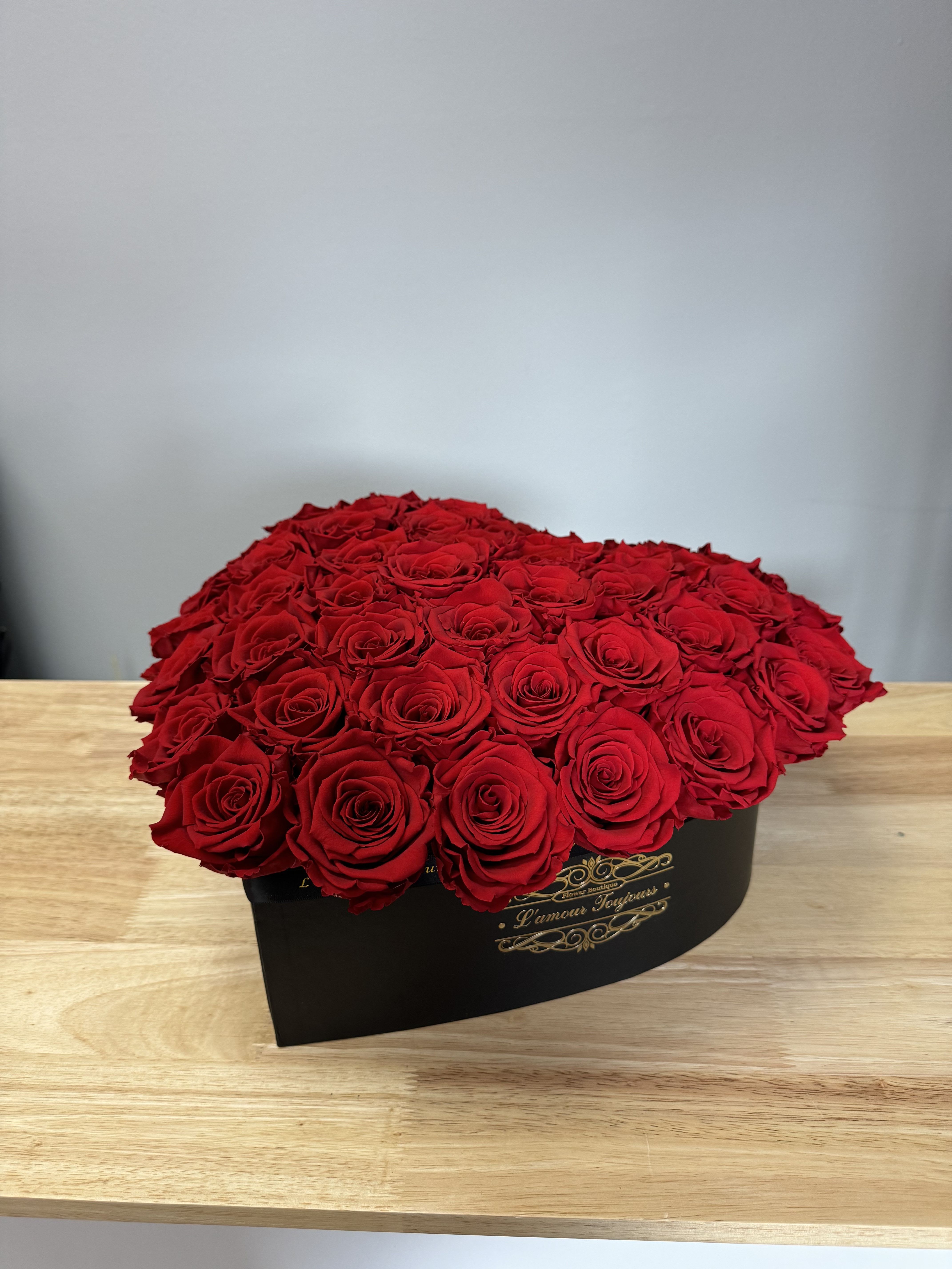Large red rose arrangement in a black hat box on a wooden table