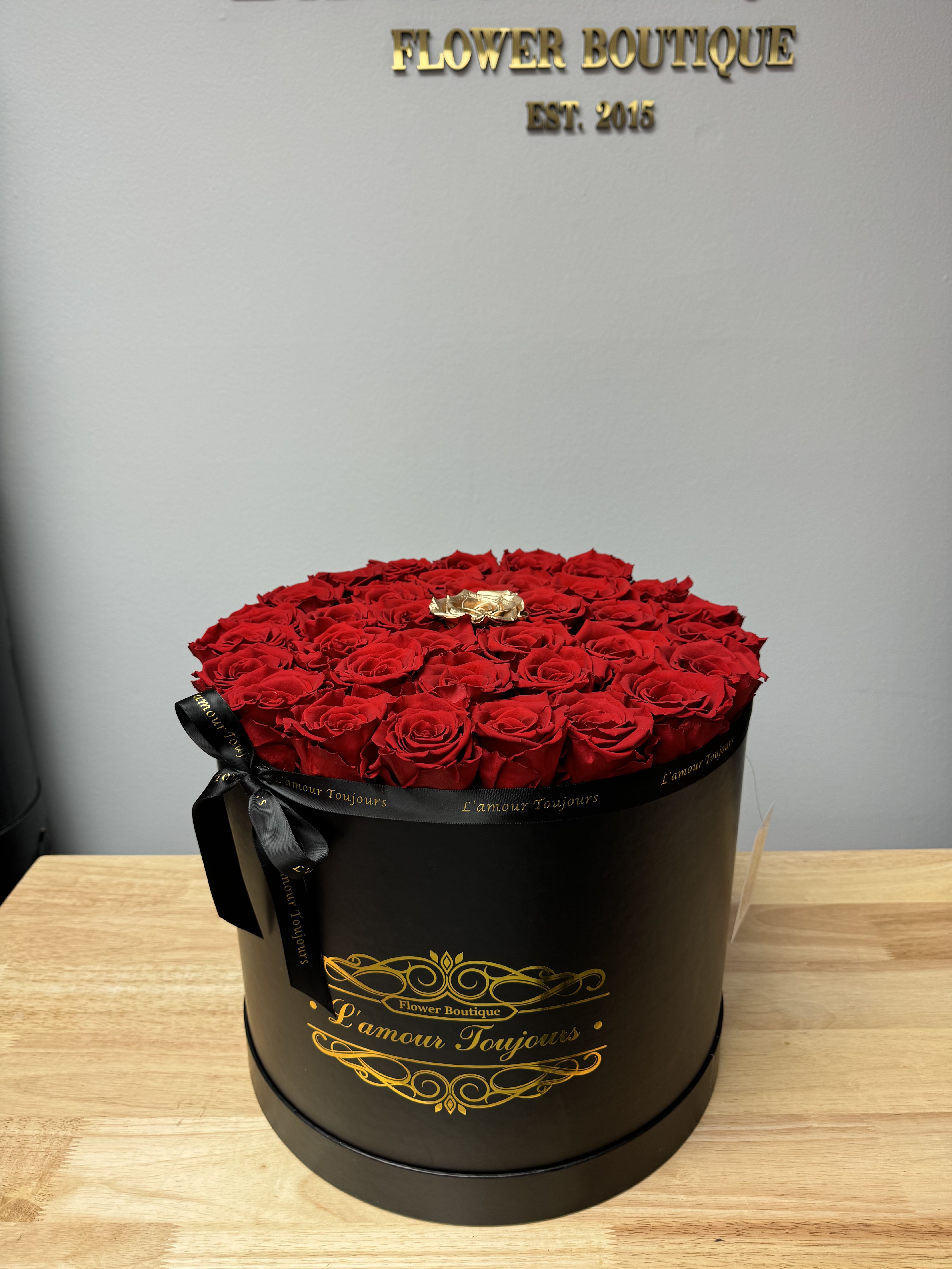 Round black hatbox filled with red roses and one gold rose on a wooden table