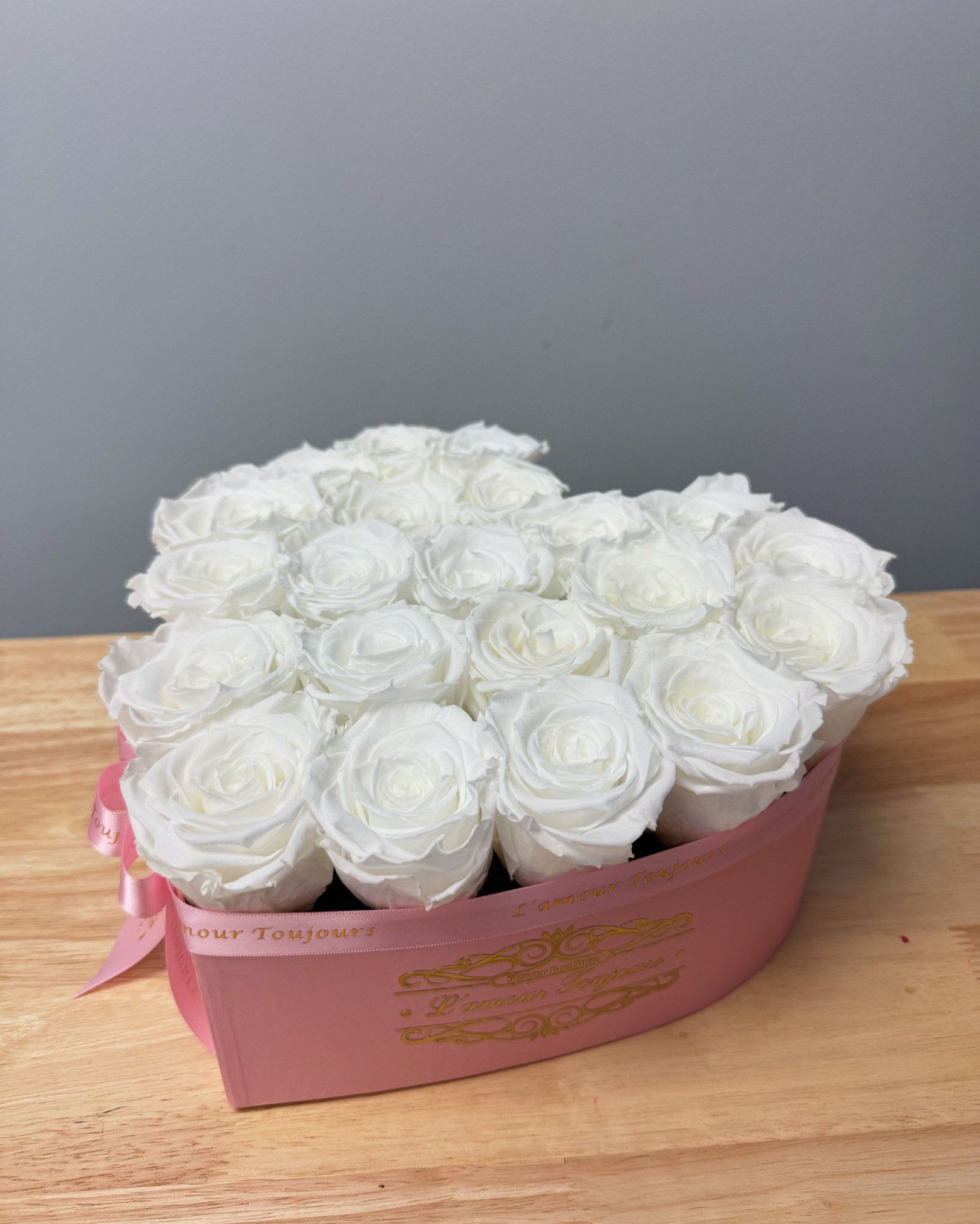 Heart-shaped pink box filled with tightly packed white roses on a wooden surface
