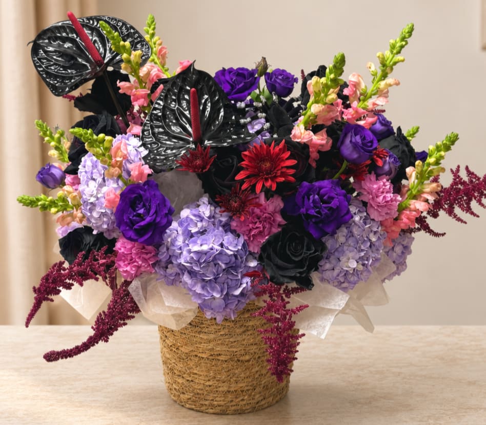 Purple and pink floral arrangement in a woven basket with black anthuriums
