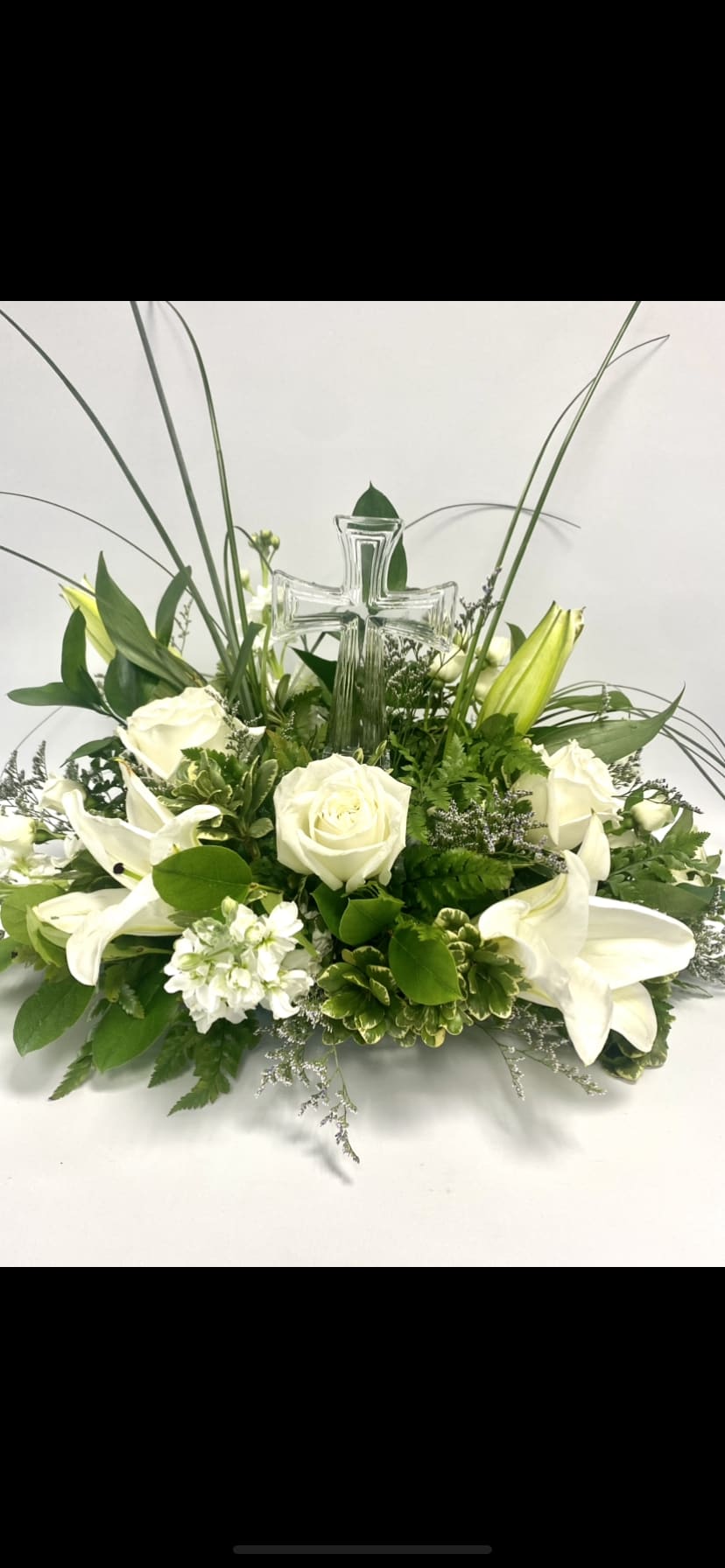 White roses and lilies arranged around a clear glass cross