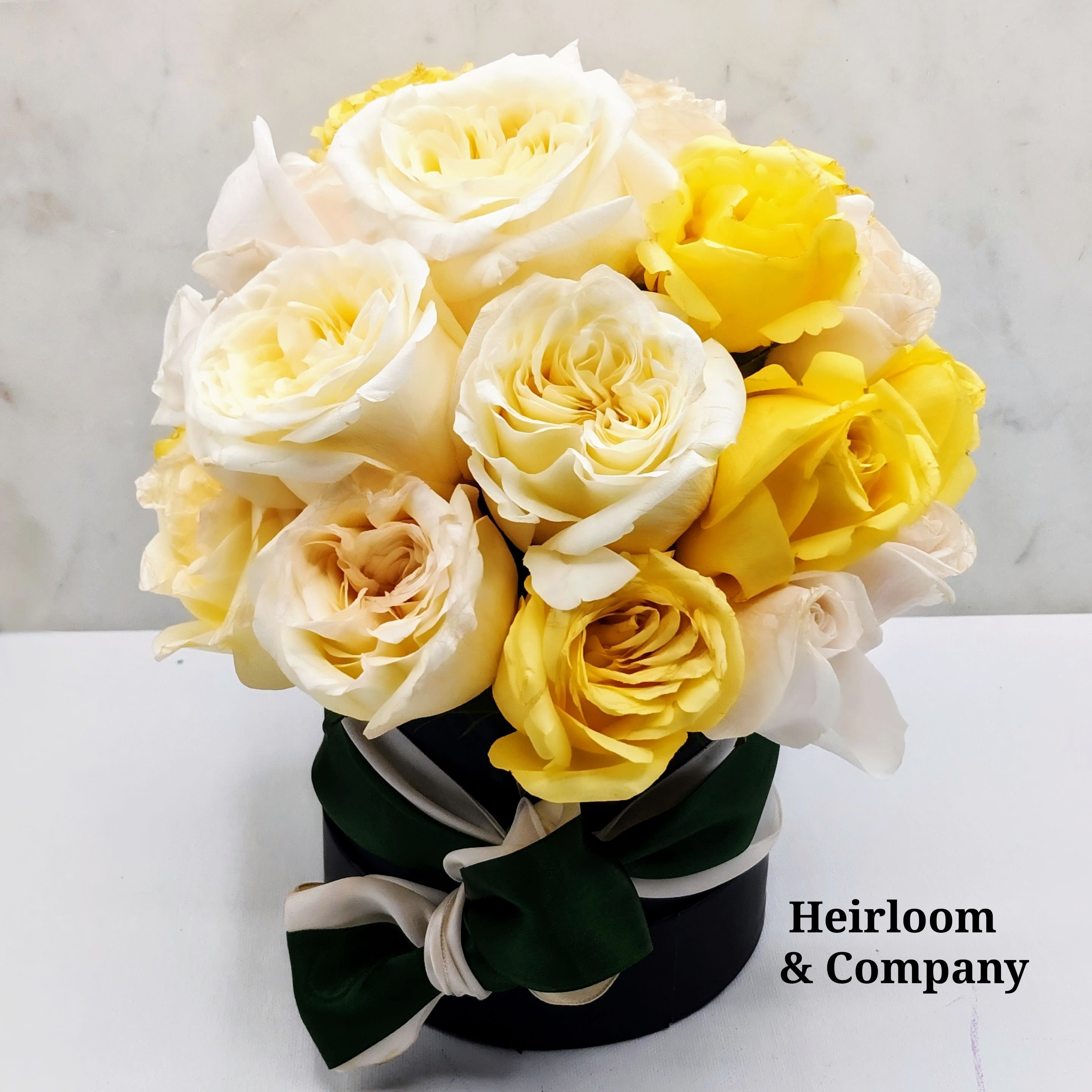 Bouquet of cream and yellow roses in a black hat box with ribbon