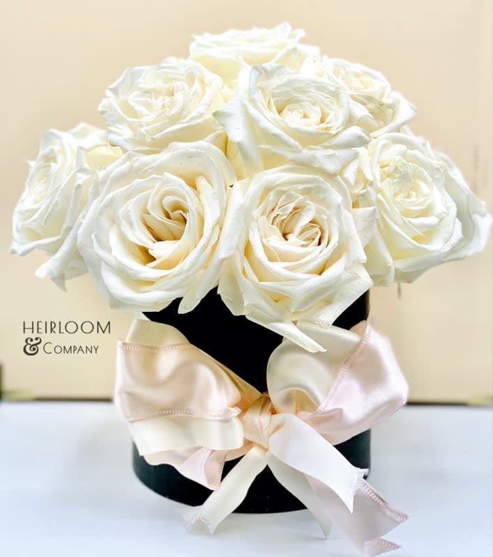 White roses arranged in a black box with a pale satin bow