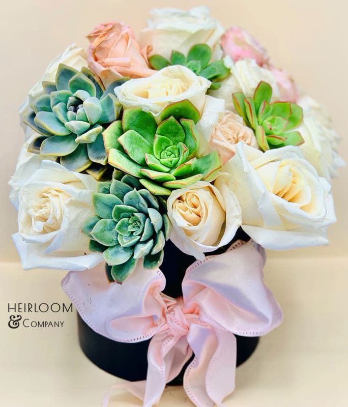 Bouquet of white roses and succulents in a black hatbox with a pink ribbon