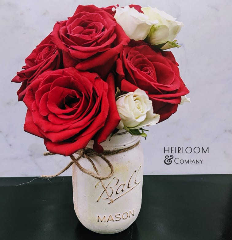 Red and white roses in a white mason jar vase
