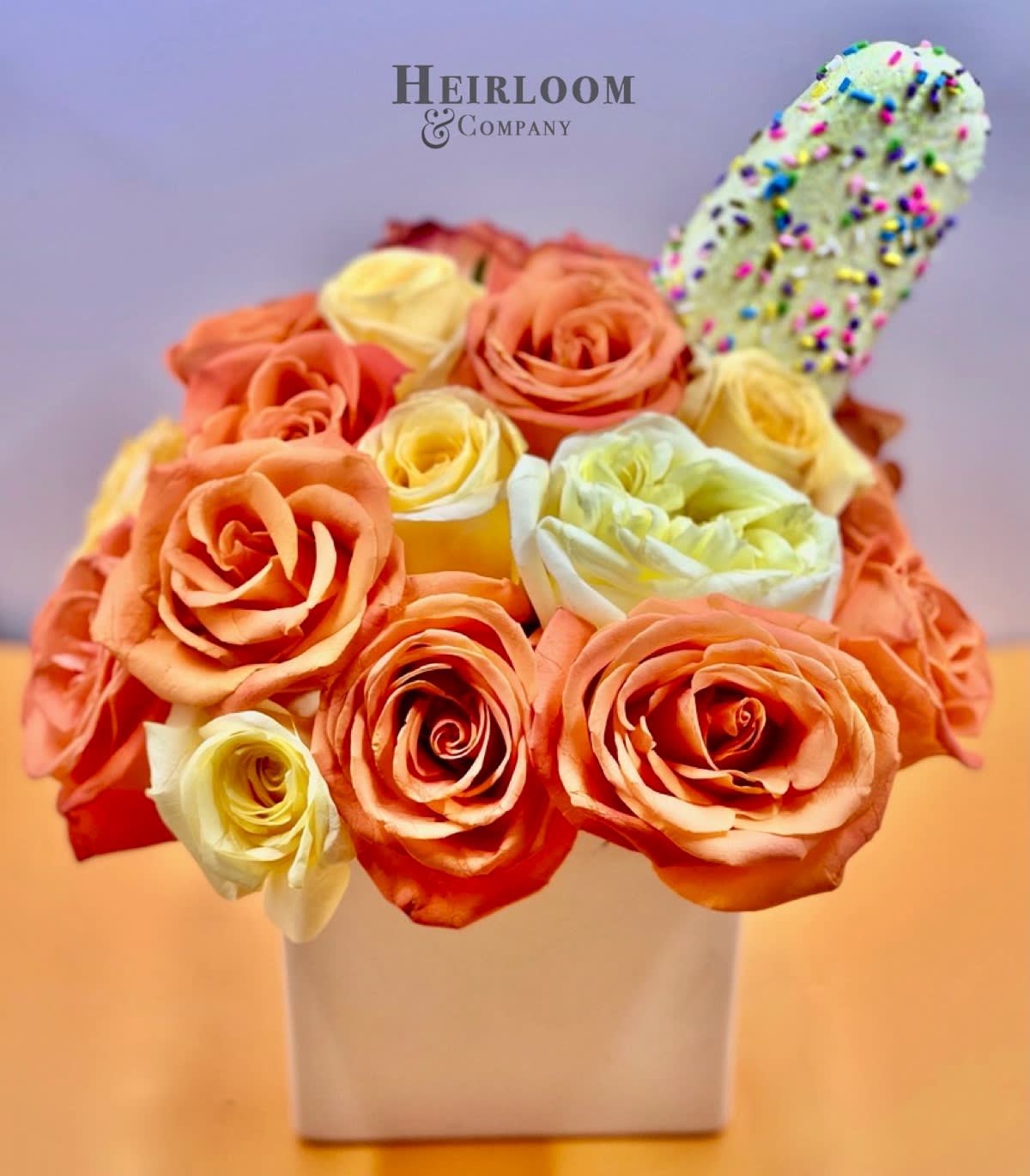 Orange and cream roses in a white square vase with a sprinkle-covered treat