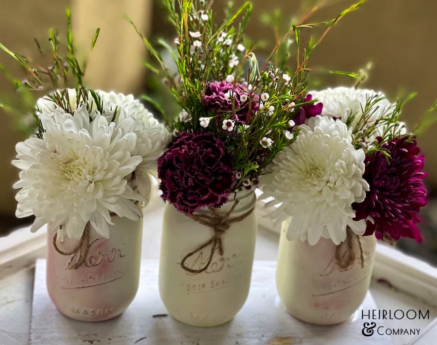 Three mason jars holding white and burgundy flowers