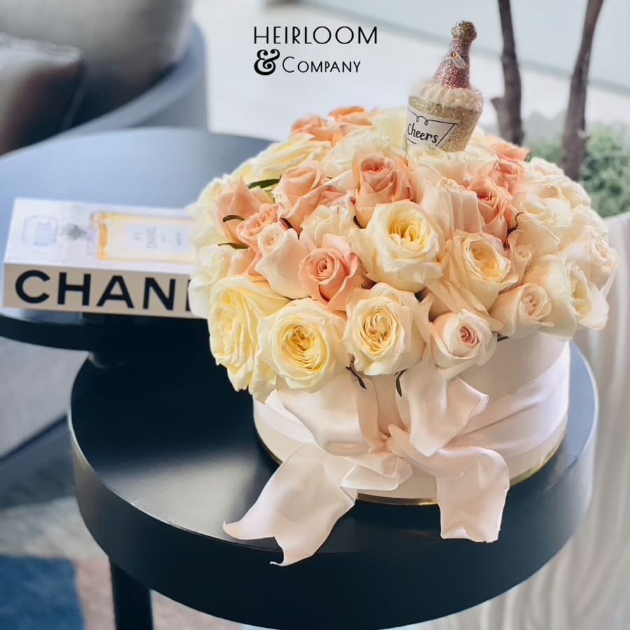 Round bouquet of pale peach and cream roses with a small champagne bottle topper