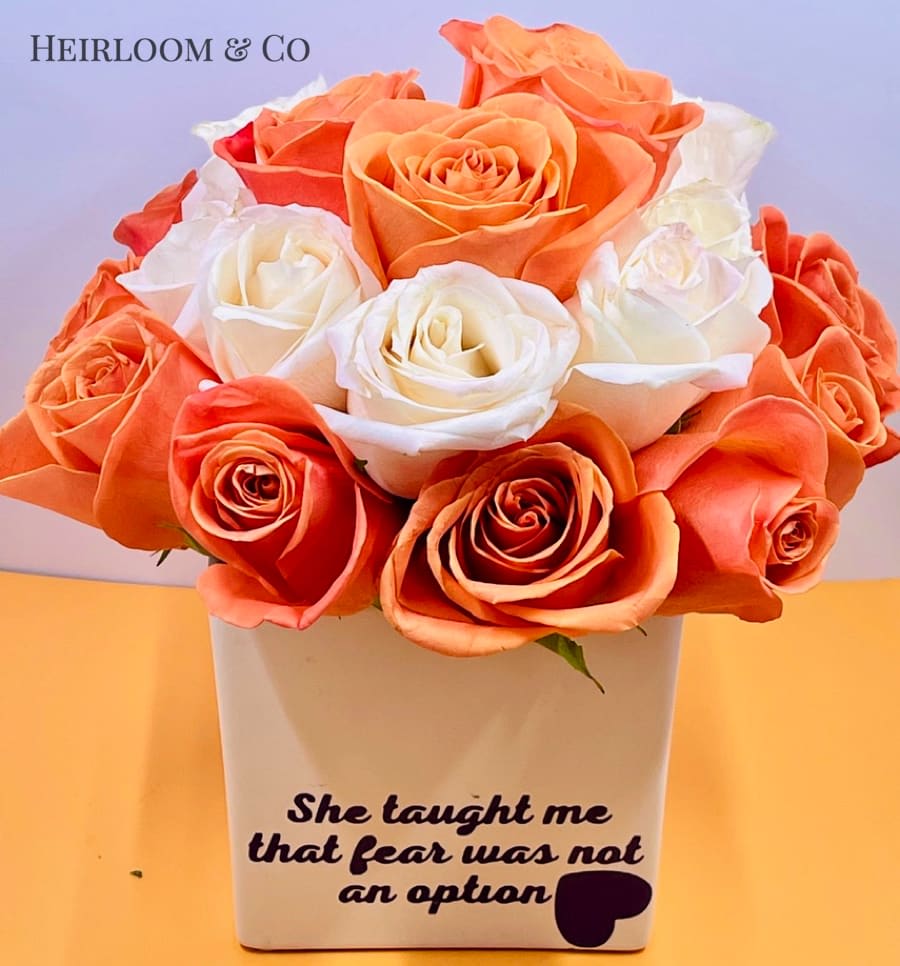 Orange and white roses arranged in a white vase with printed text