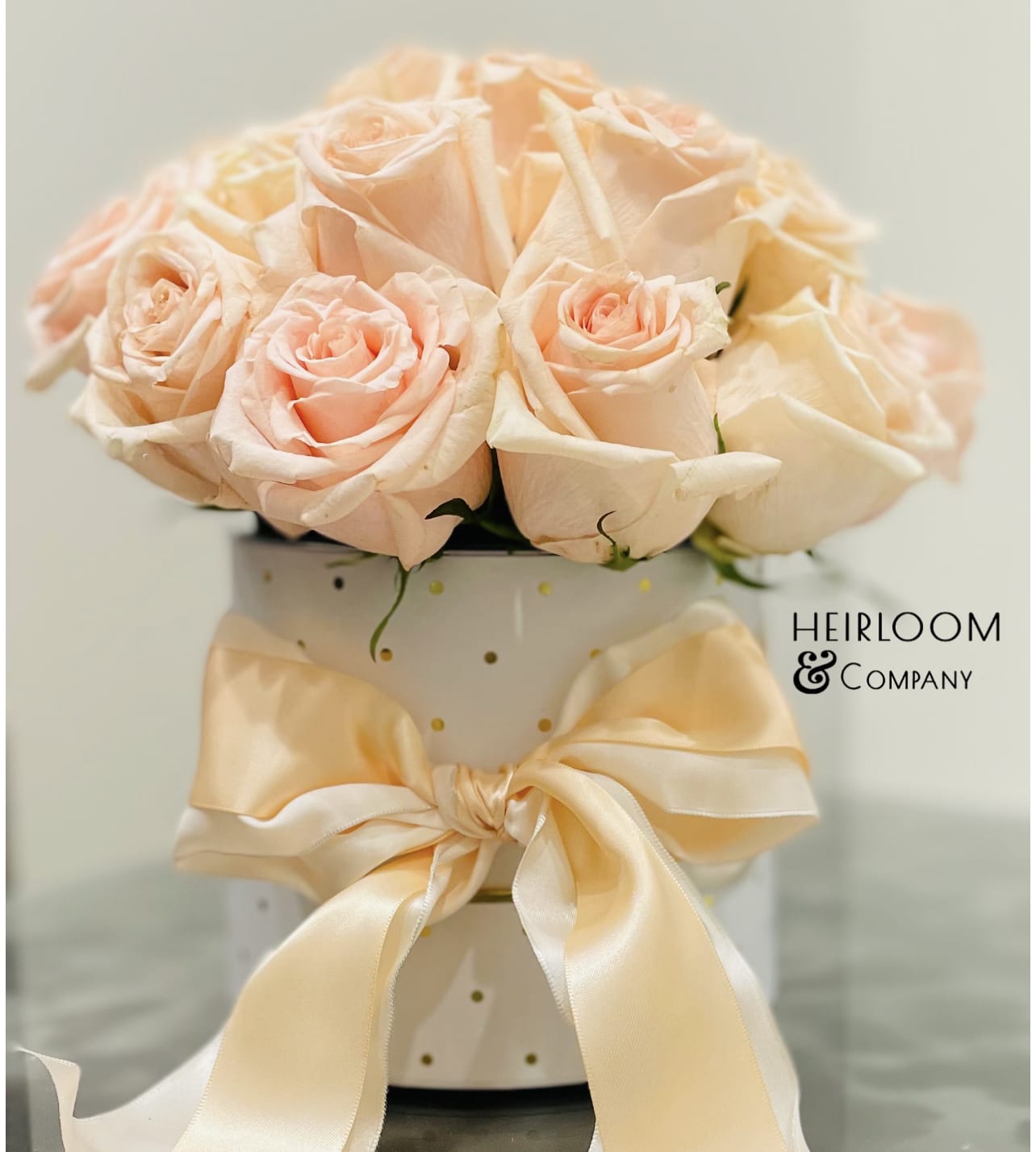 Peach roses arranged in a white polka-dot hatbox with a satin bow