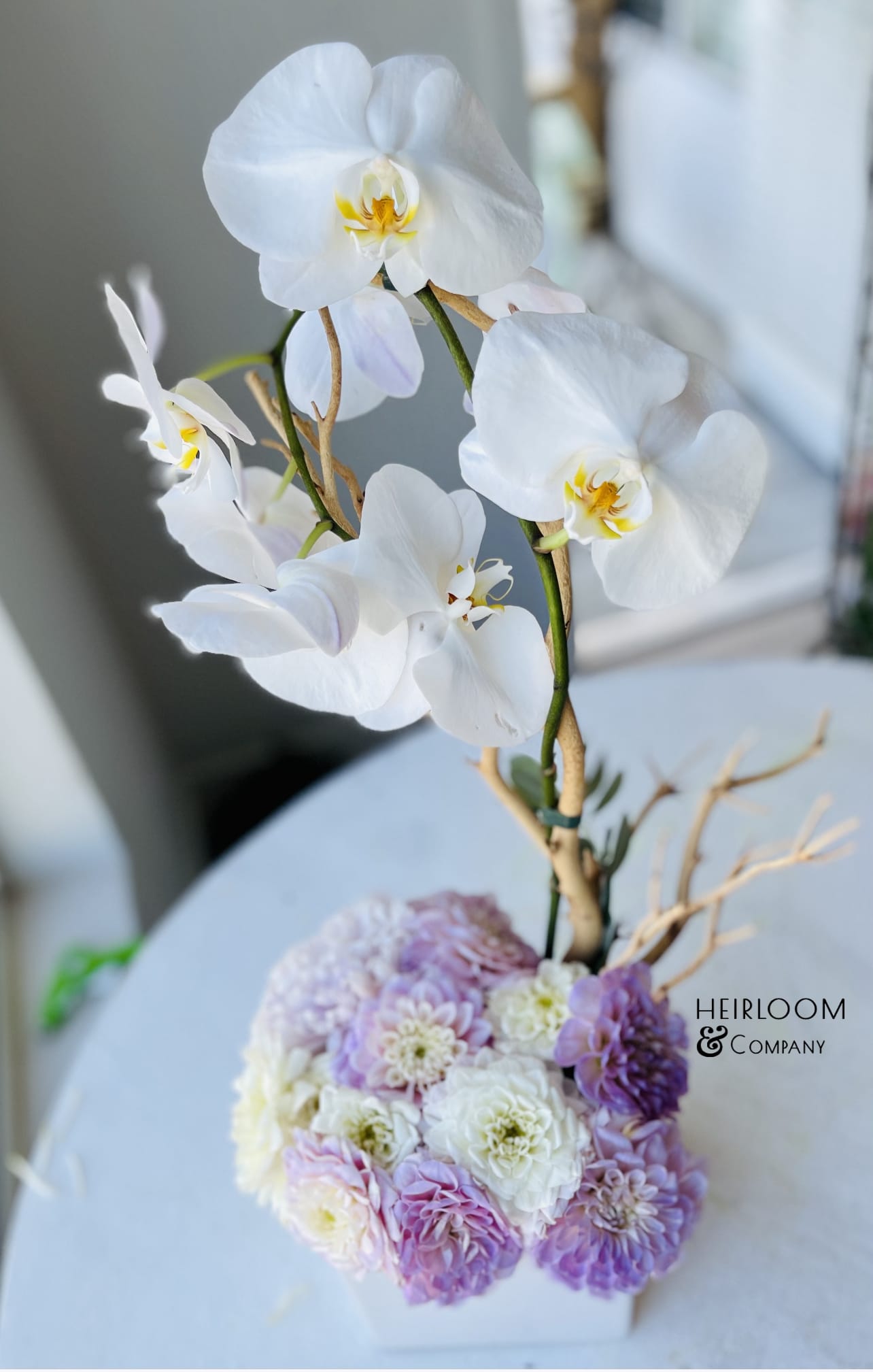 White orchids above a pastel pink and lavender floral arrangement in a white vase